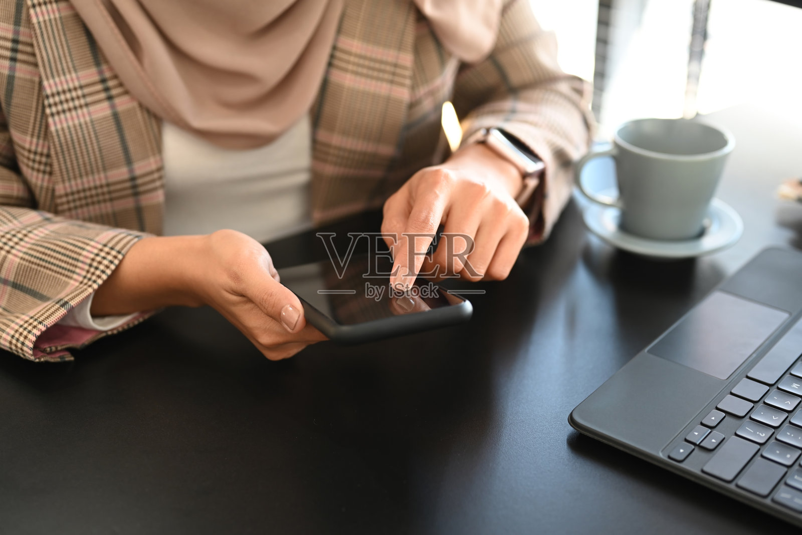 年轻的女商人使用智能手机和坐在办公室的笔记本电脑前的特写。照片摄影图片