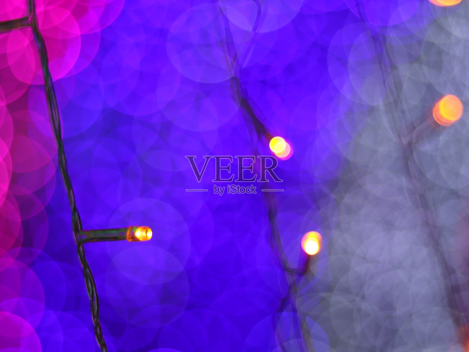 摘要散景灯模糊了背景,圣诞树上的灯泡为庆祝季节用粉色、紫色和白色的彩色散焦圈作为背景邀请卡。多色彩虹散景。照片摄影图片