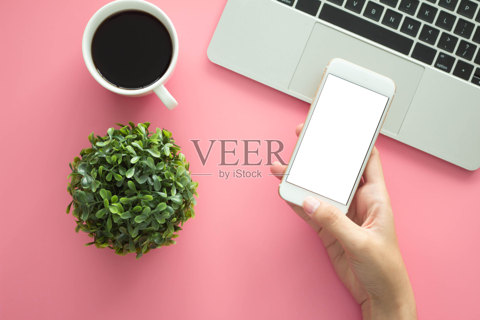 男人手持空白显示智能手机现代粉色办公桌与笔记本电脑和其他用品与一杯咖啡输入文本在复制空间俯视图,平躺。照片摄影图片