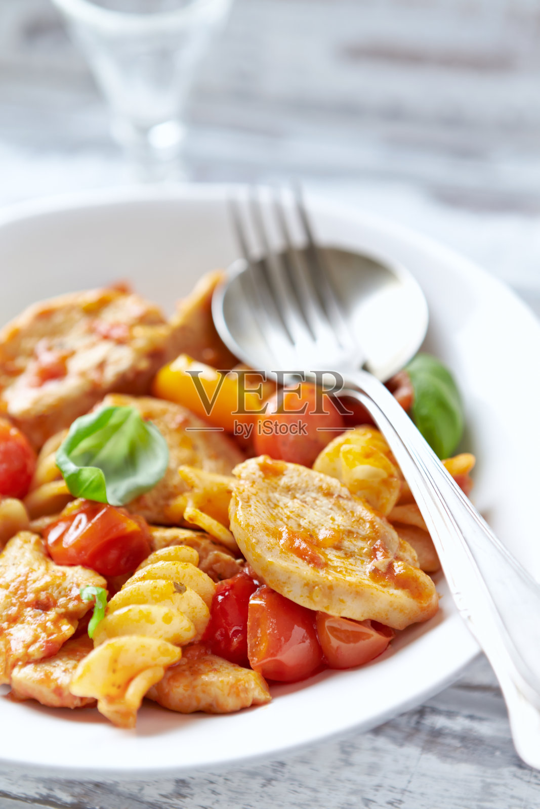 意大利面配鸡胸肉、圣女果和新鲜罗勒。明亮的木制背景。关闭了。照片摄影图片