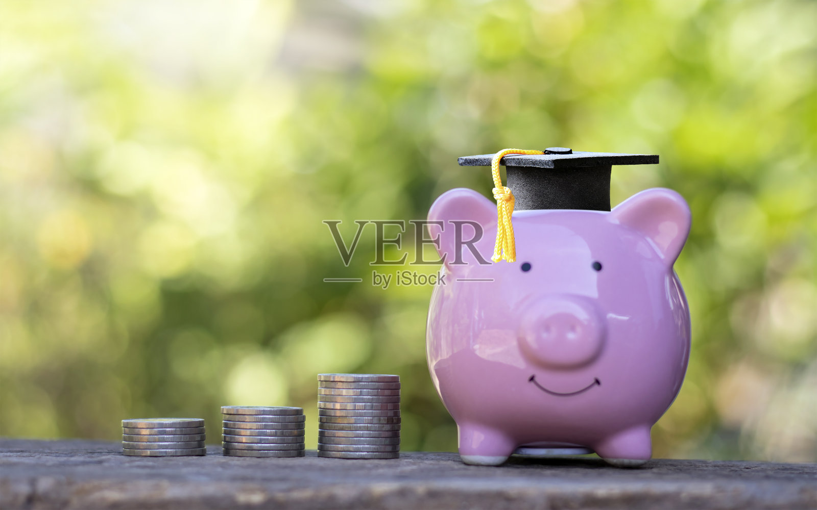 毕业生的帽子放在储蓄罐上,硬币堆放在木地板上。教育理念与教育储蓄。照片摄影图片