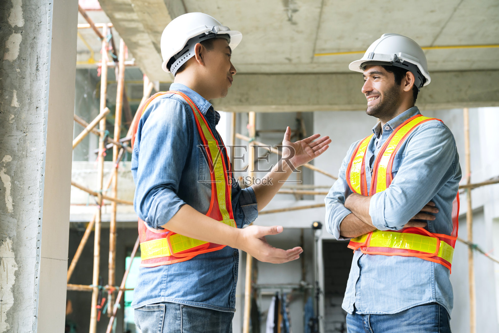 年轻的亚洲工程师和白种人工程师同事在工地视察,一起用笔记本电脑和图纸在建筑工地讨论。家居装修理念概念照片摄影图片