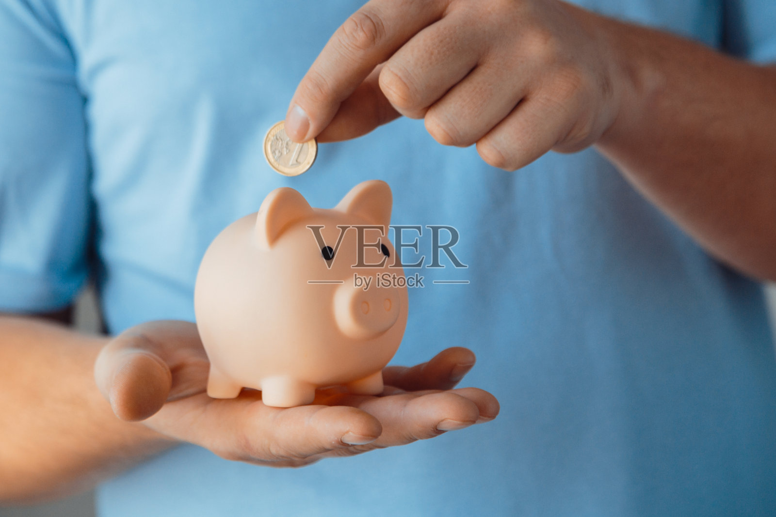 男人的手把一枚硬币放在一个粉红色的储蓄罐里。选择性和柔和的焦点复古色调照片摄影图片