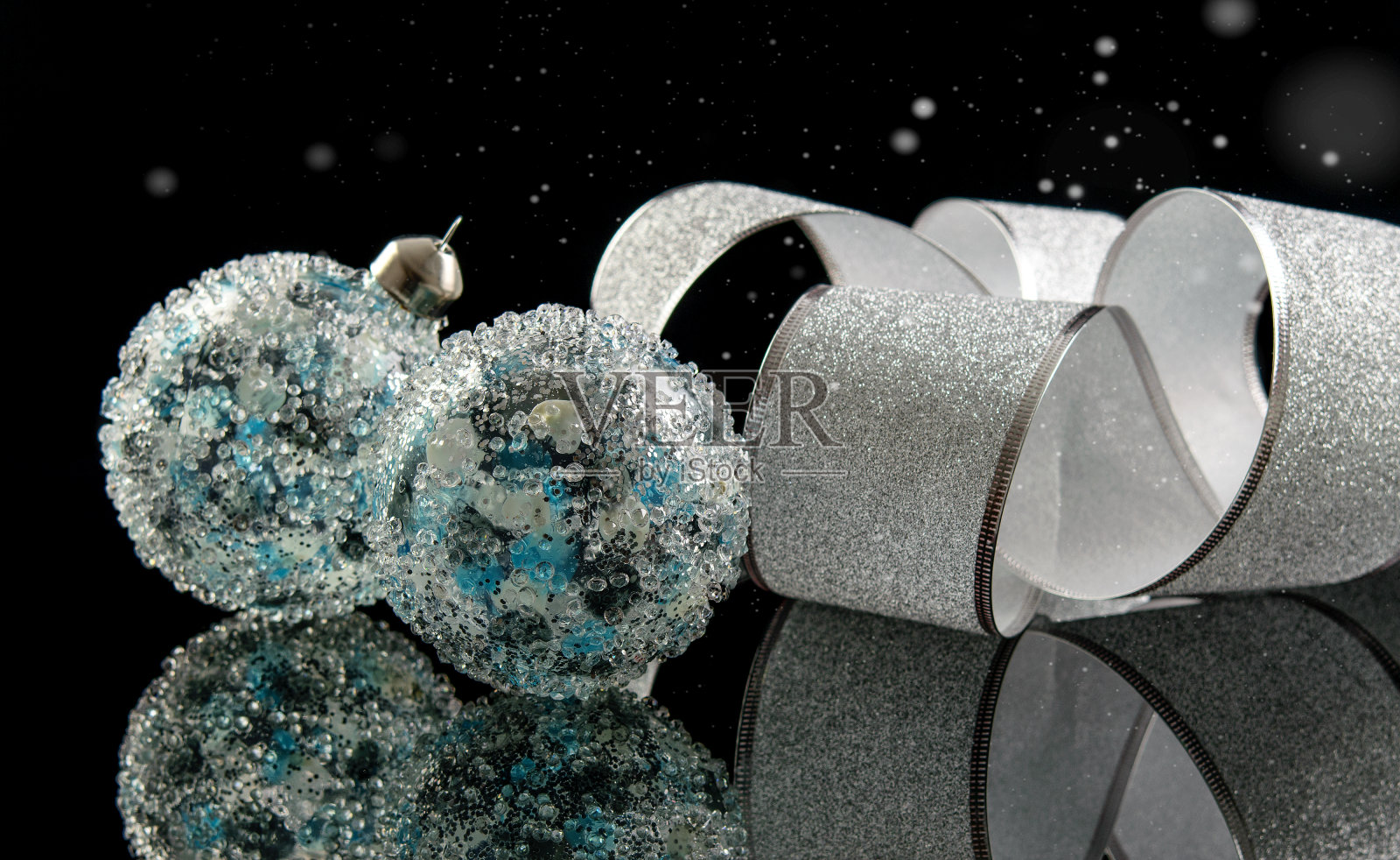 蓝色的白色玻璃球和宽大优雅的银色丝带在黑色的反光背景上。圣诞节和新年的概念。照片摄影图片