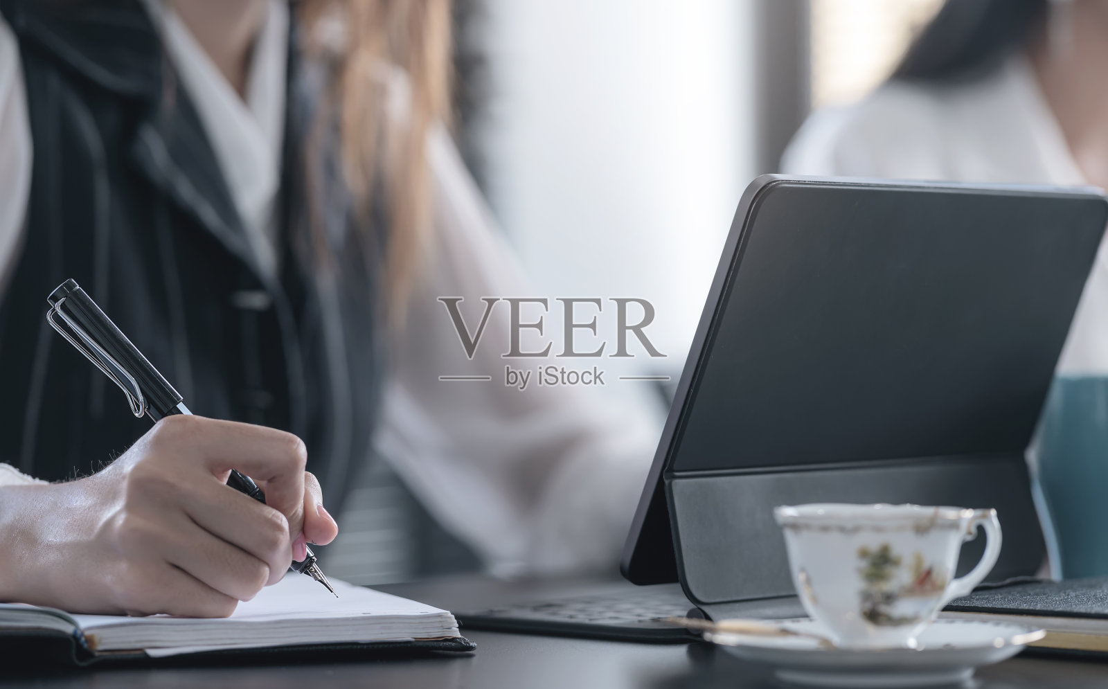 一个女人坐在办公桌前用钢笔在笔记本上写字的镜头。照片摄影图片