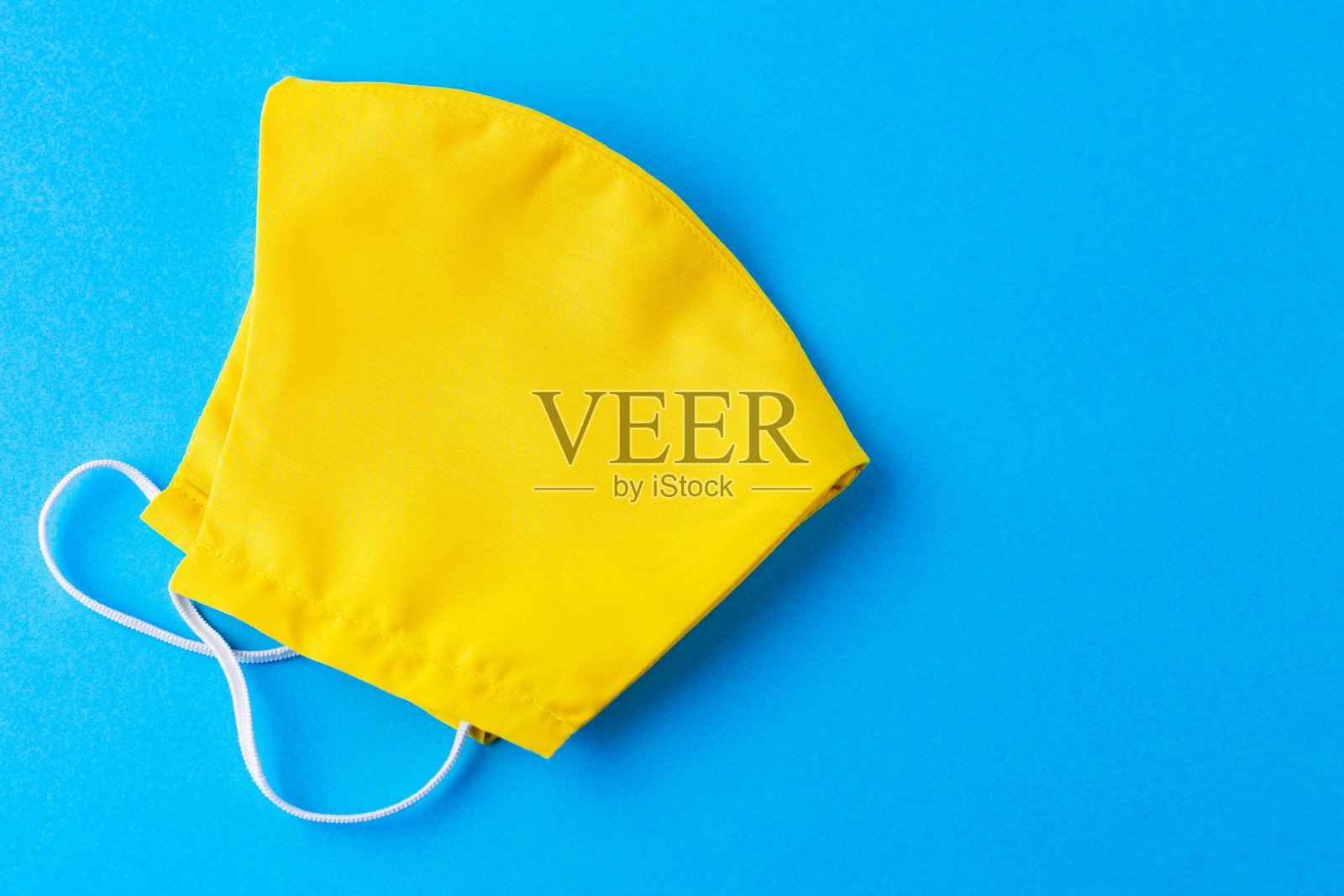 用黄色棉布制成的可重复使用的口罩。面对防毒面具。黄色防护面具,蓝色背景。波普艺术风格。前视图。本空间照片摄影图片