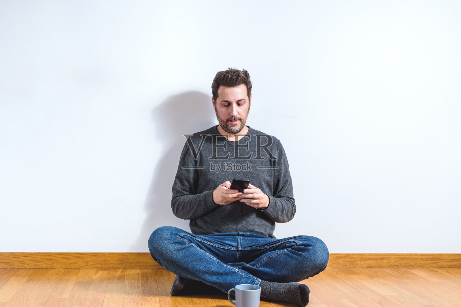 一个40多岁的年轻人坐在空荡荡的公寓地板上玩着智能手机照片摄影图片