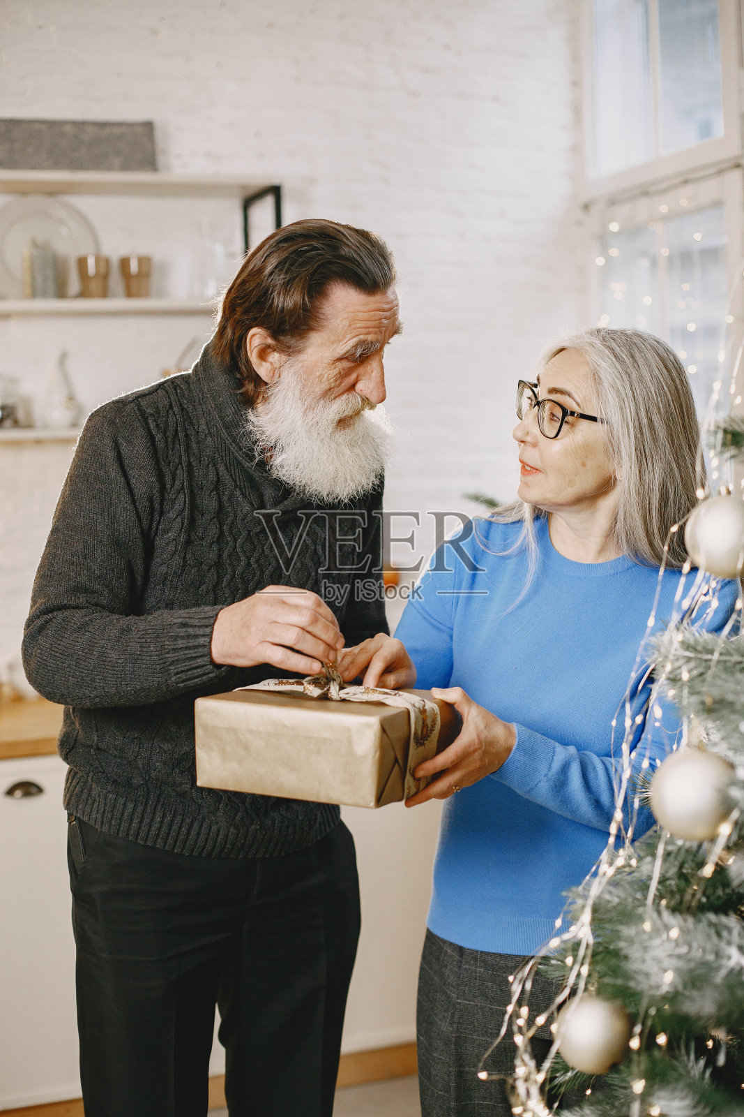 一对老年夫妇在圣诞树旁拿着礼物照片摄影图片