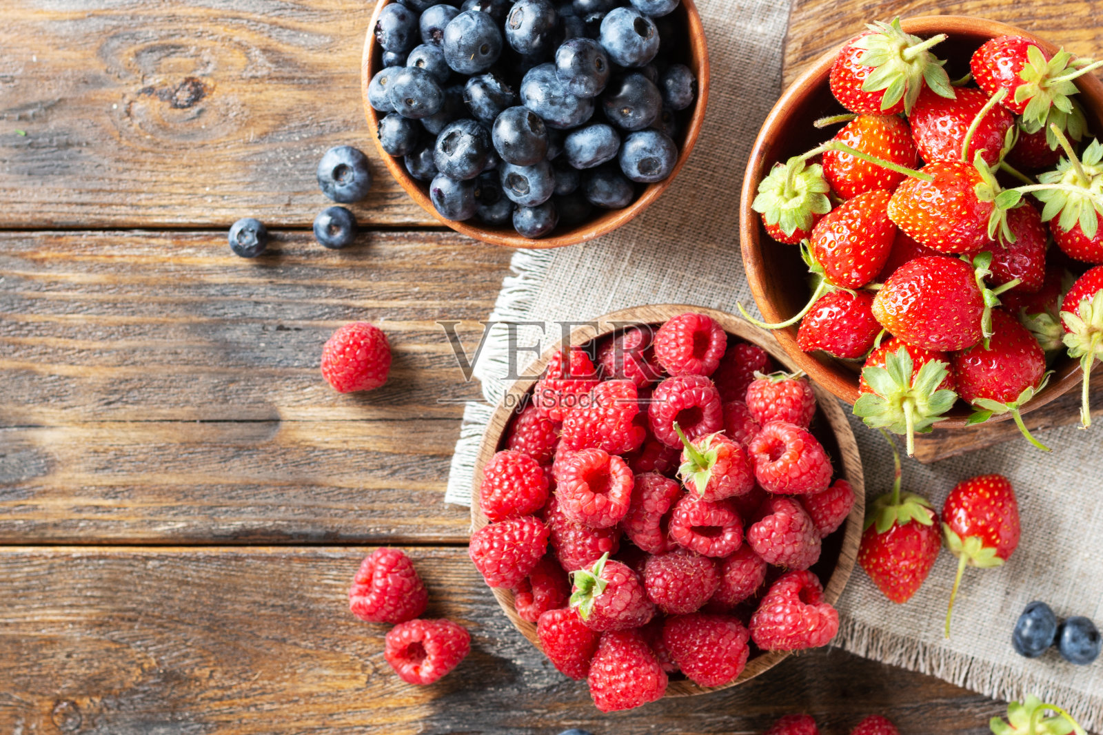 浆果。各种浆果装在木碗里,放在棕色的木桌上。用碗盛草莓、覆盆子和蓝莓照片摄影图片