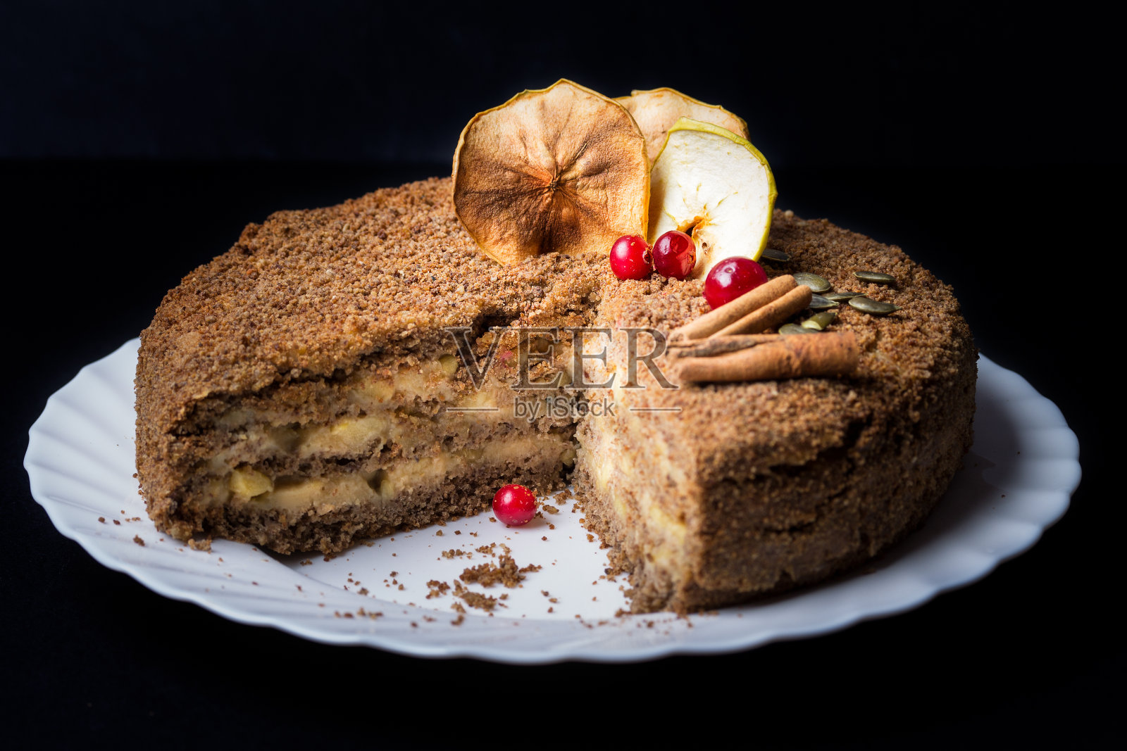 在前台的白色盘子上放着一块无麸质、无鸡蛋的果仁蛋糕,里面是奶油苹果馅。照片摄影图片