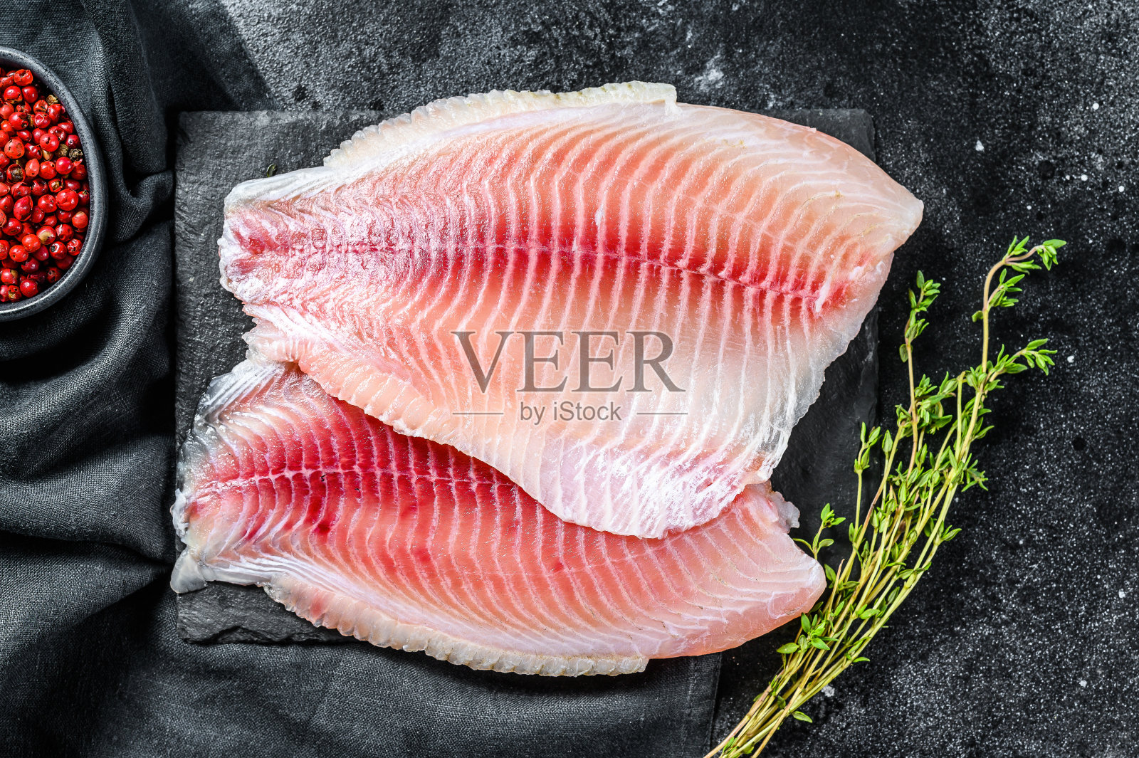 切菜板上的新鲜罗非鱼片配百里香。黑色背景。俯视图照片摄影图片