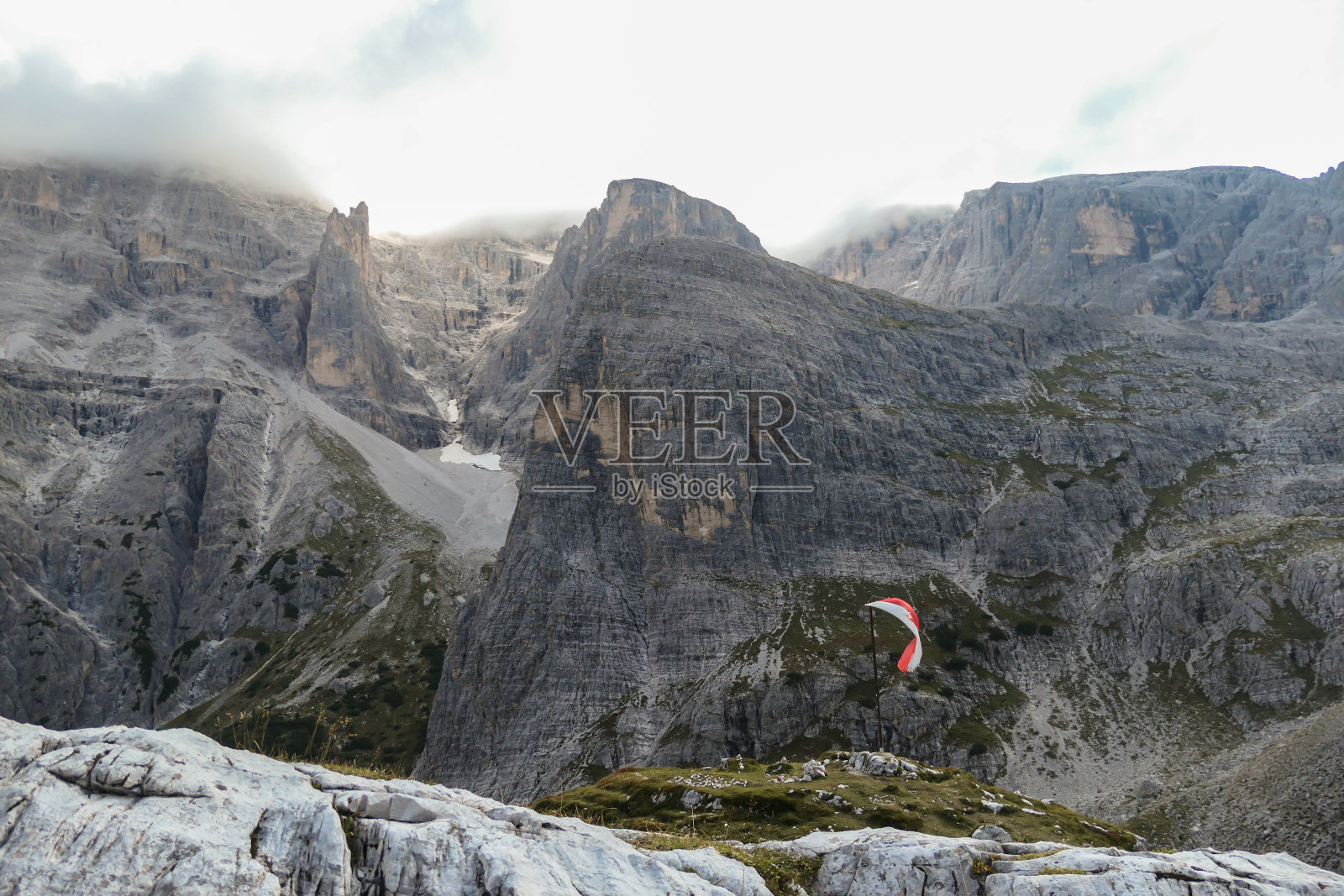 Oberbachernspitze -意大利Dolomites的一面Tirolian旗帜在风中飘扬。有许多高耸的山峰覆盖着云照片摄影图片