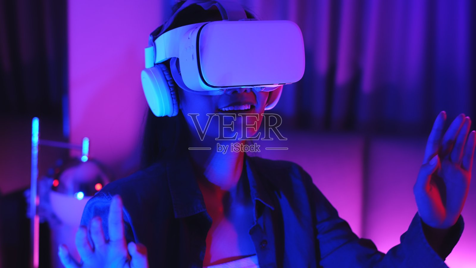 年轻的亚洲女性正在使用虚拟现实耳机。霓虹灯工作室肖像。虚拟现实、模拟、游戏和未来技术的概念。亚洲女人在卧室玩游戏。照片摄影图片