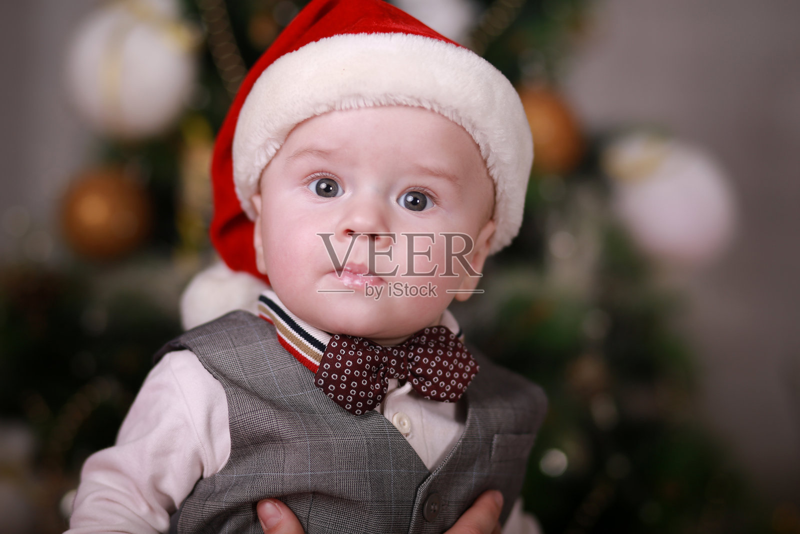 在圣诞树的背景上,有趣的小男孩戴着圣诞老人的帽子照片摄影图片
