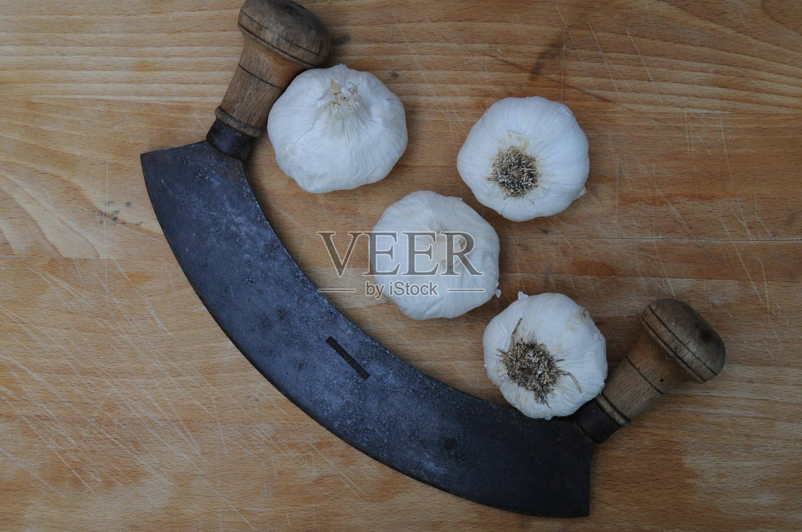 大蒜和半月形刀放在用过的木砧板上。照片摄影图片