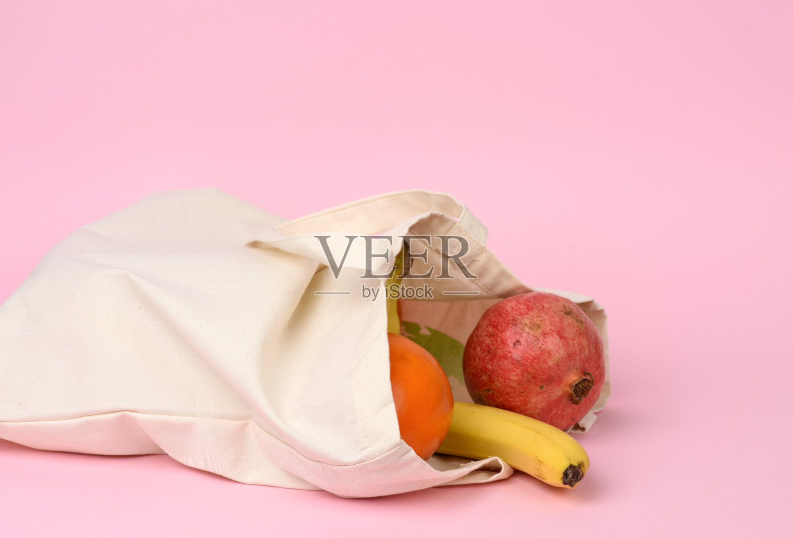 米色纺织袋与新鲜水果在粉红色的背景照片摄影图片