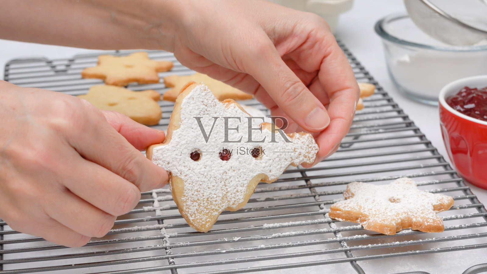 圣诞酥饼配覆盆子果酱食谱,封闭烘焙过程。烤饼乾放在冷却架上,女人的手照片摄影图片