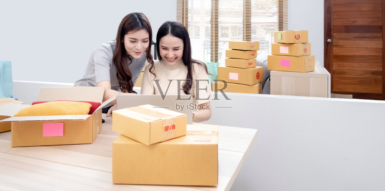 两位美丽的亚洲女性正在网上用笔记本电脑查看订单。用快乐的笑脸包装纸盒,成为网上新常态照片摄影图片