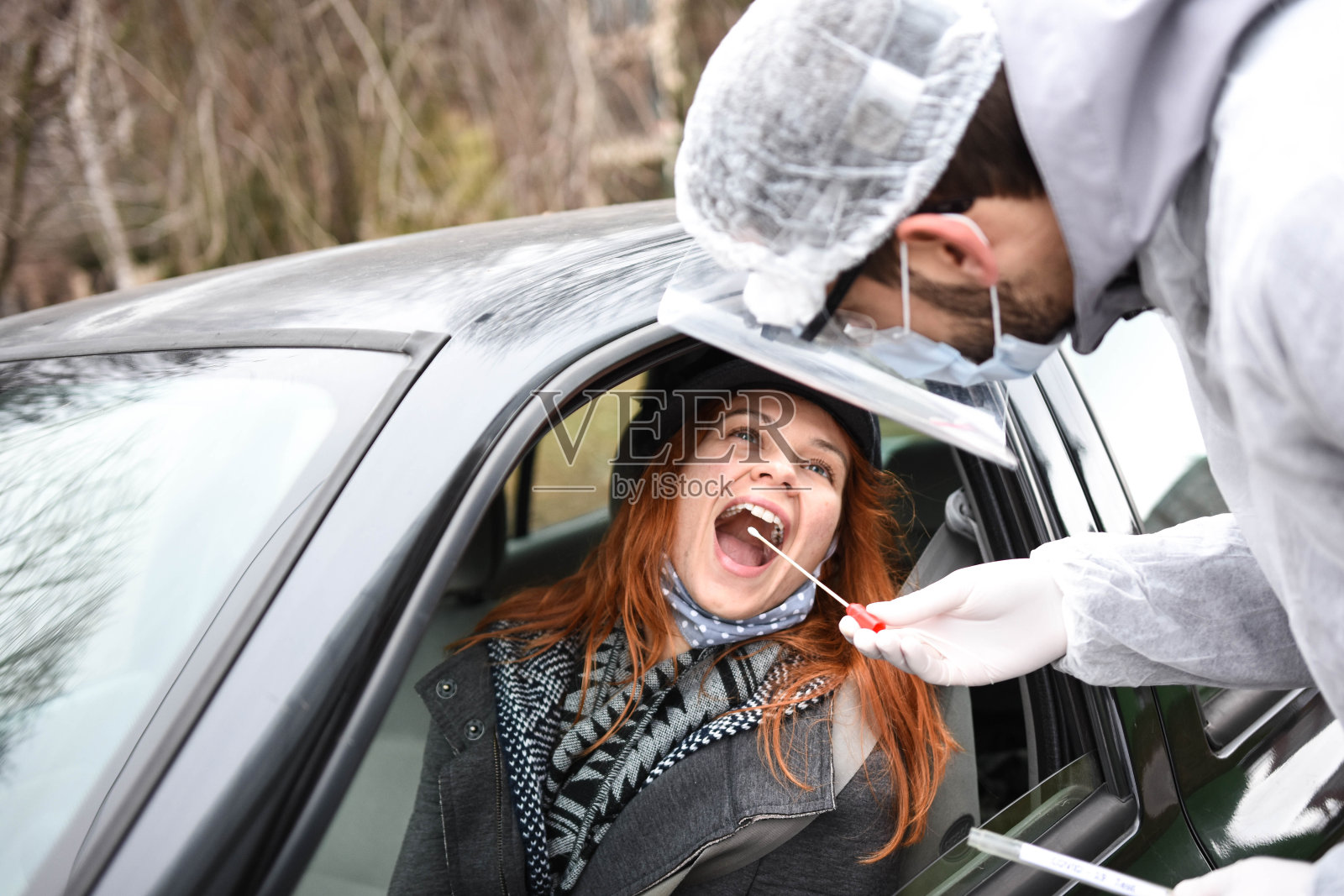 身穿防护服的医生在街上用口腔拭子擦拭一个人,以检测他是否可能感染冠状病毒。司机通过城市新冠肺炎检测中心照片摄影图片