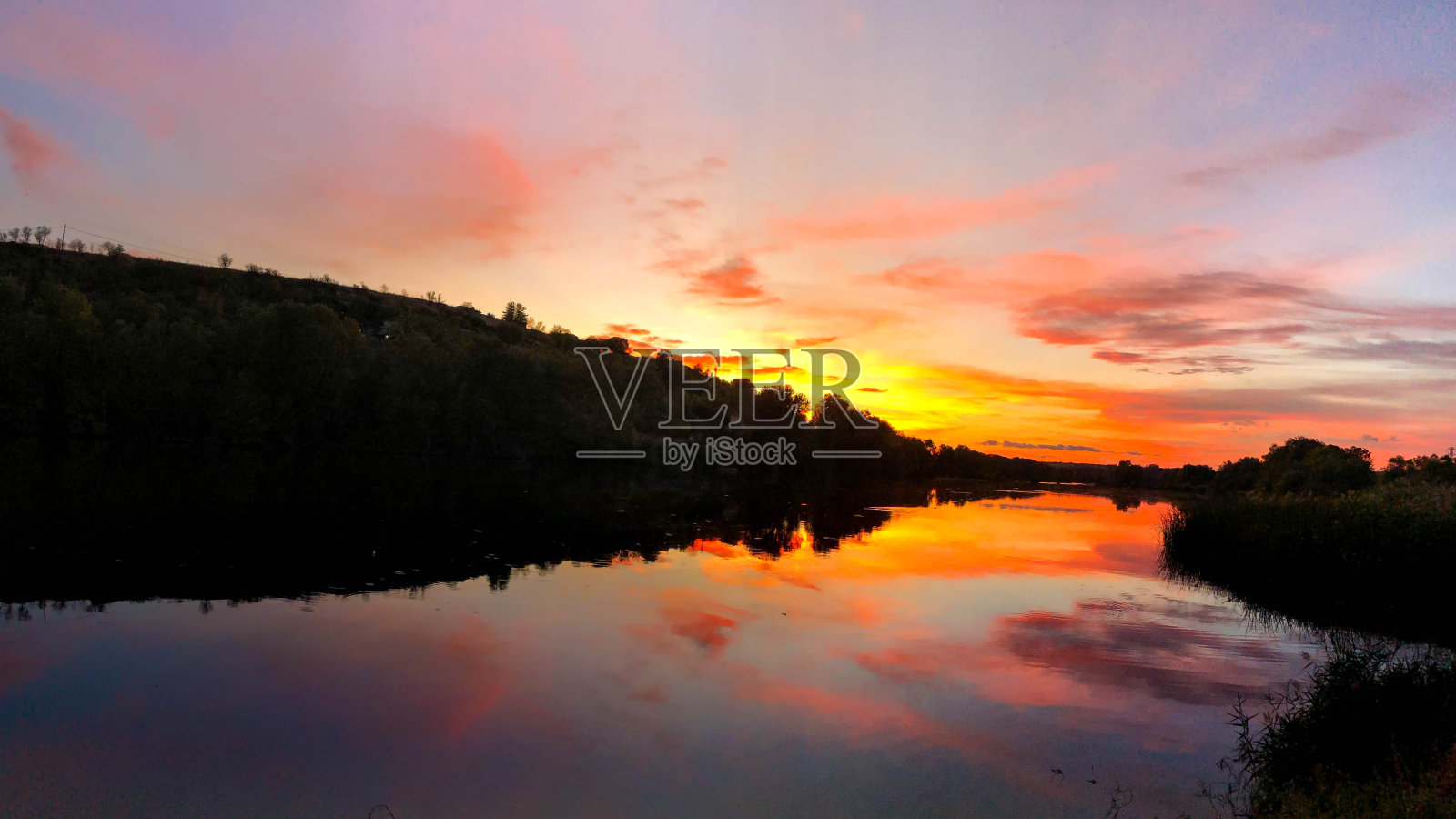 水平全景的金色日落与山的剪影在背景。红色、橙色、紫色和水中的倒影。非常戏剧性的日落场景照片摄影图片