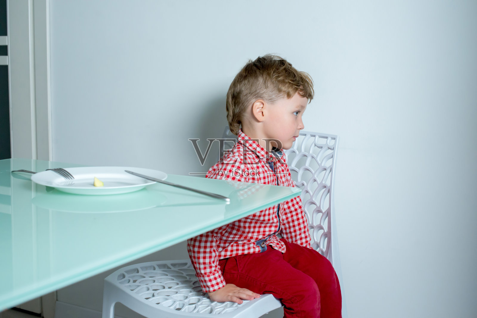 男孩坐在厨房里不肯吃东西。照片摄影图片