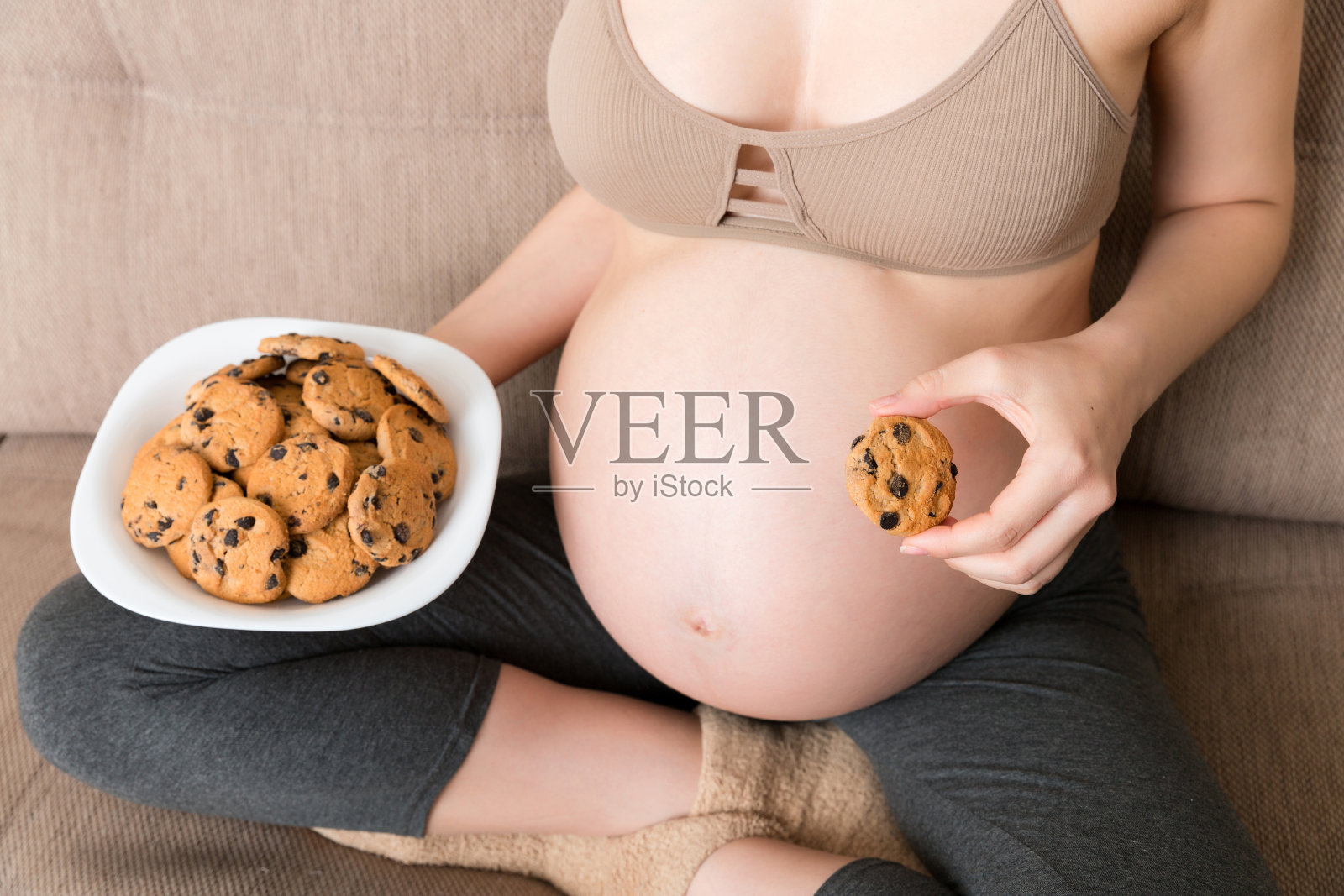 近距离的孕妇喜欢吃饼干休息在家里的沙发上。怀孕期间不健康的甜点概念照片摄影图片