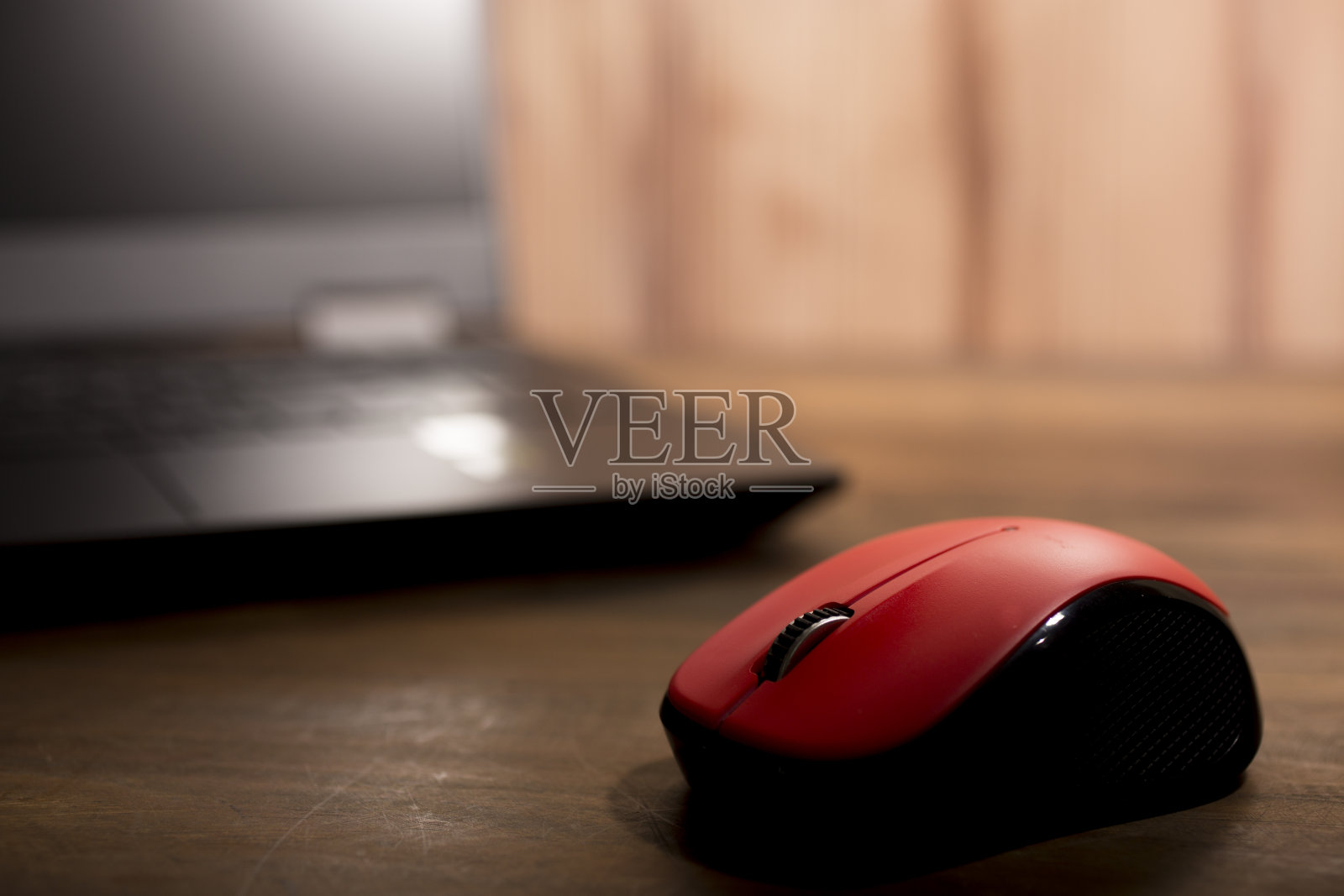 木制书桌上放着笔记本电脑和红色鼠标。照片摄影图片