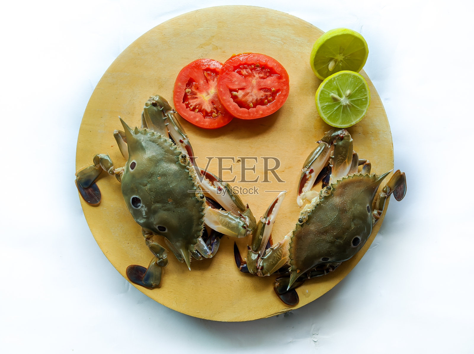 精选鲜三斑梭子蟹放在木垫上,饰以柠檬片和番茄片。孤立在白色背景上。照片摄影图片