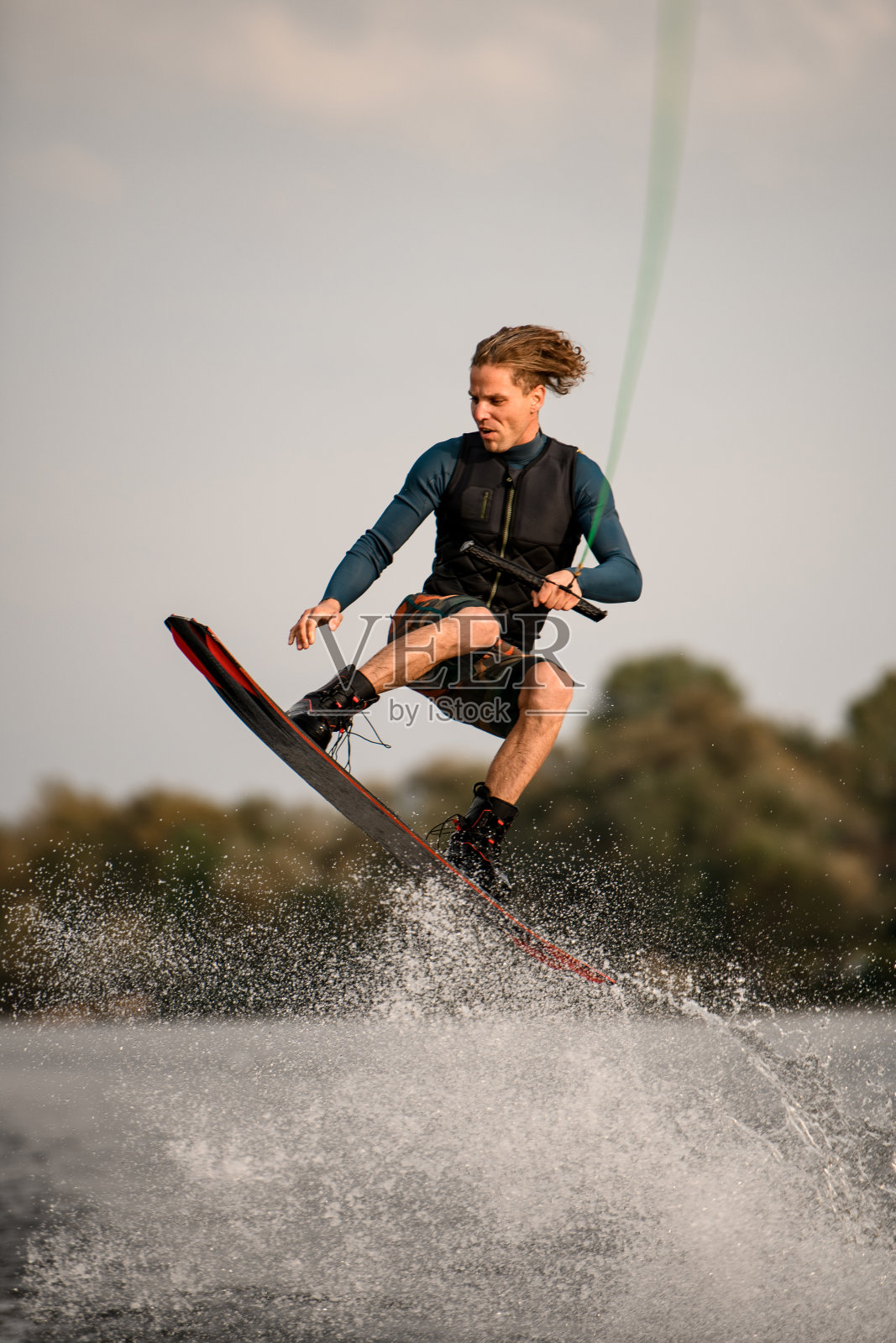 男子熟练地跳过溅起水花的尾流板。背景是天空和绿树照片摄影图片