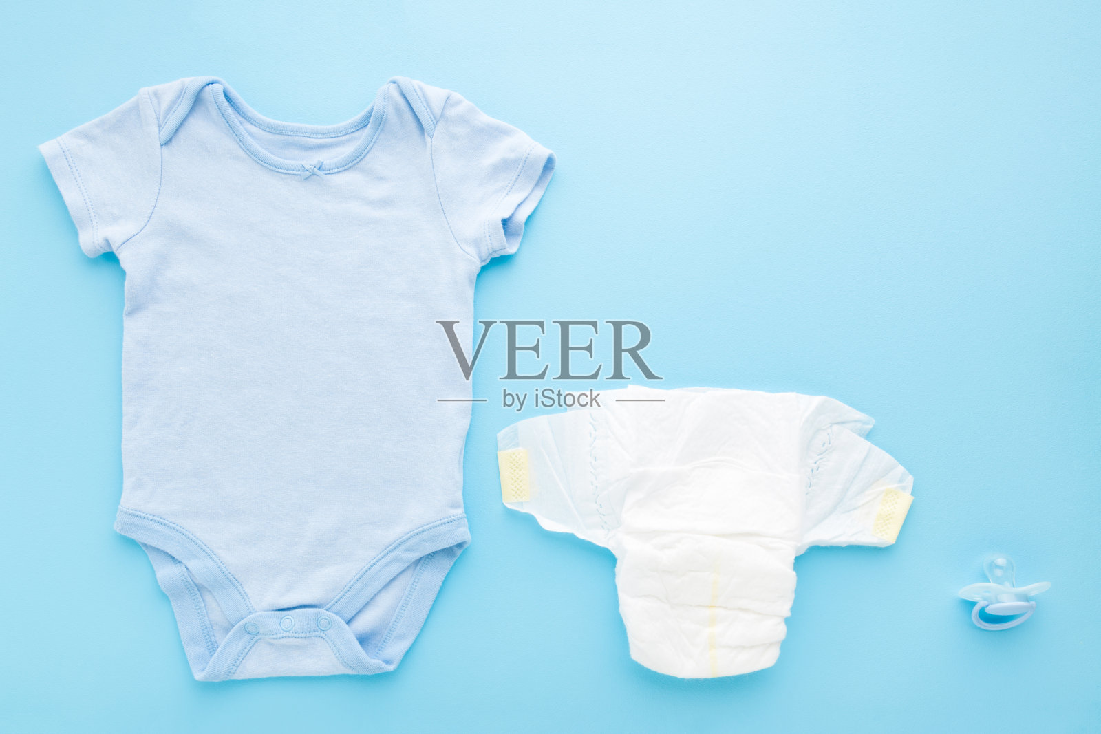 婴儿紧身衣,白色尿布和奶嘴在浅蓝色的桌子背景。柔和的颜色。特写镜头。文字或标识的空白位置。自顶向下的观点。照片摄影图片