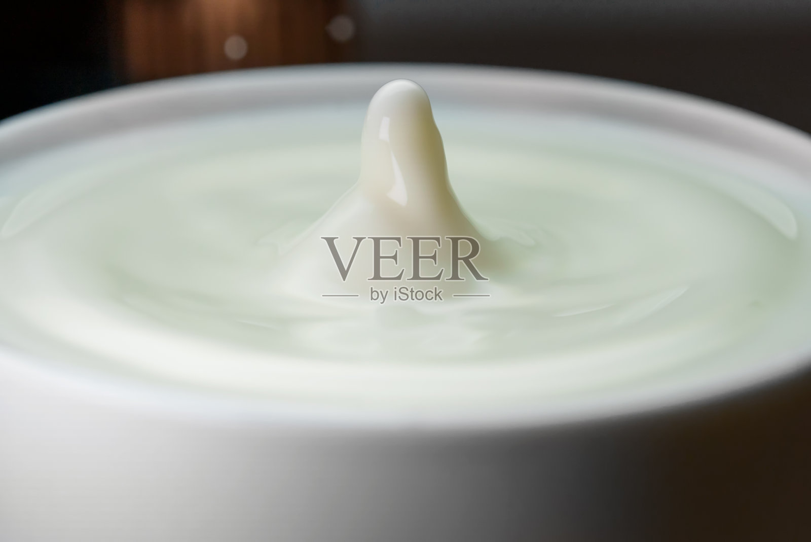 一滴牛奶掉进装满牛奶的杯子里。照片摄影图片