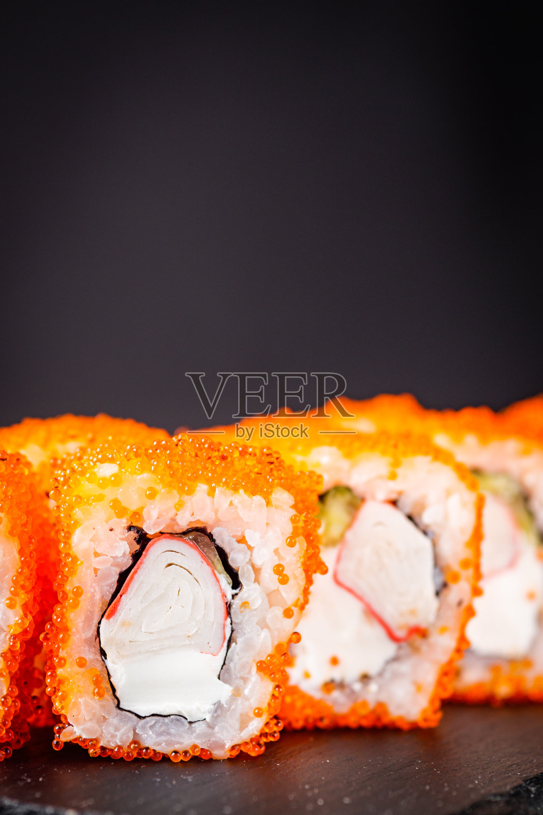 美味的加州寿司卷、芝士、黄瓜蟹和马萨戈鱼子酱放在一个黑色的石头盘子里照片摄影图片