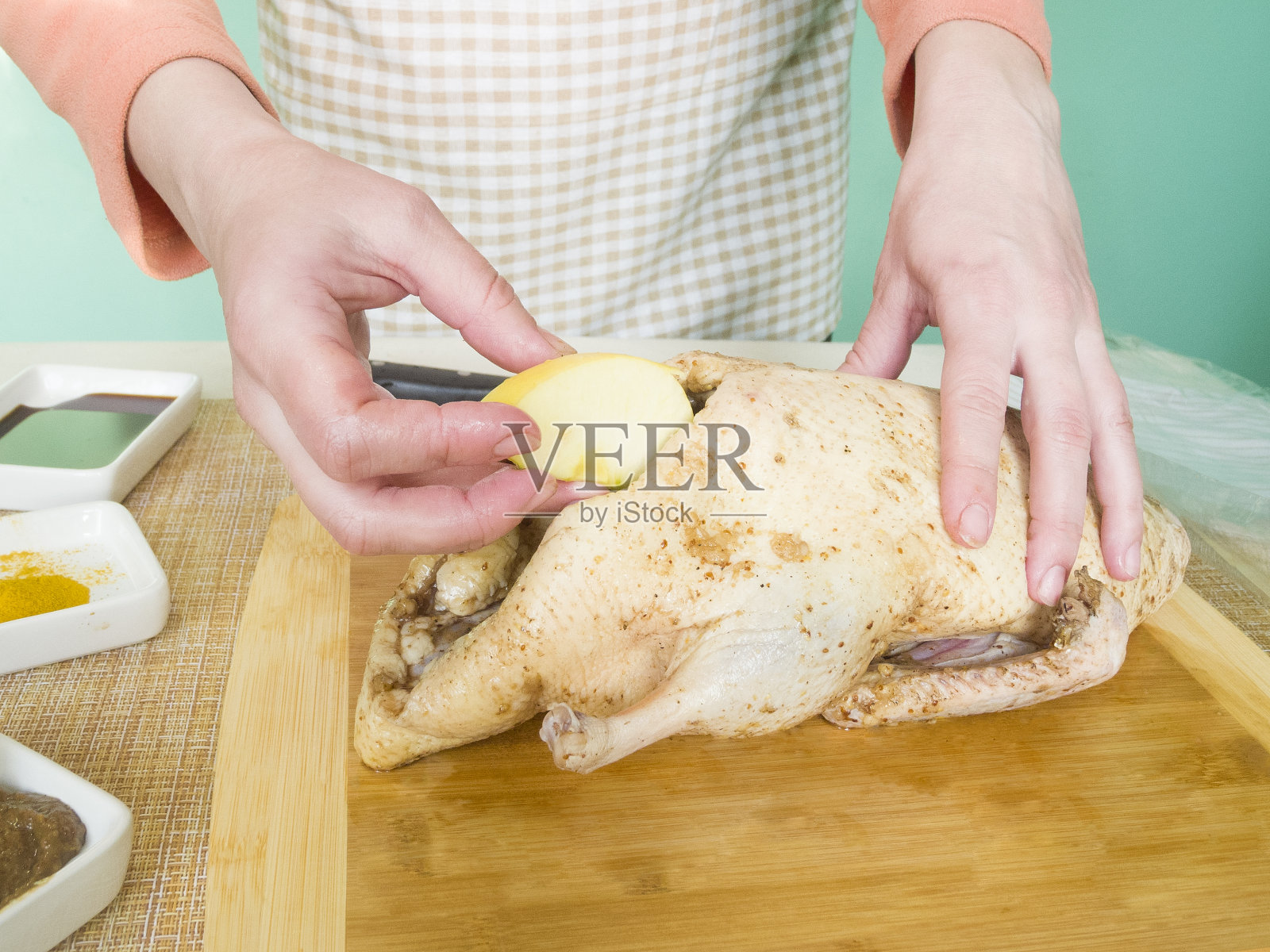 一个年轻女子在家里用苹果填满一整只鸭子作为圣诞晚餐。把鸭子抹上香料,放到烤箱里烤照片摄影图片