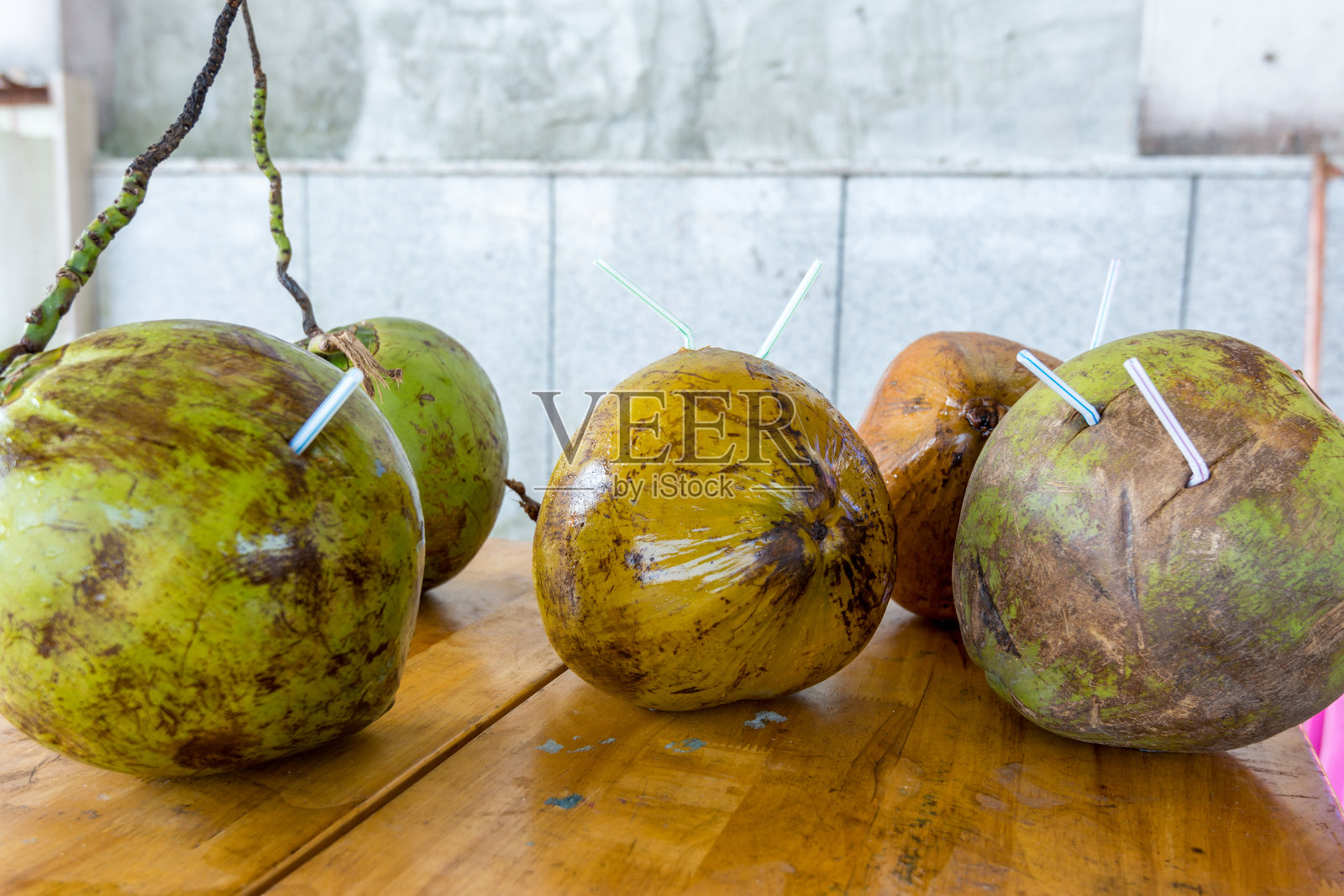 绿色的未成熟的椰子和稻草放在桌上供饮用照片摄影图片
