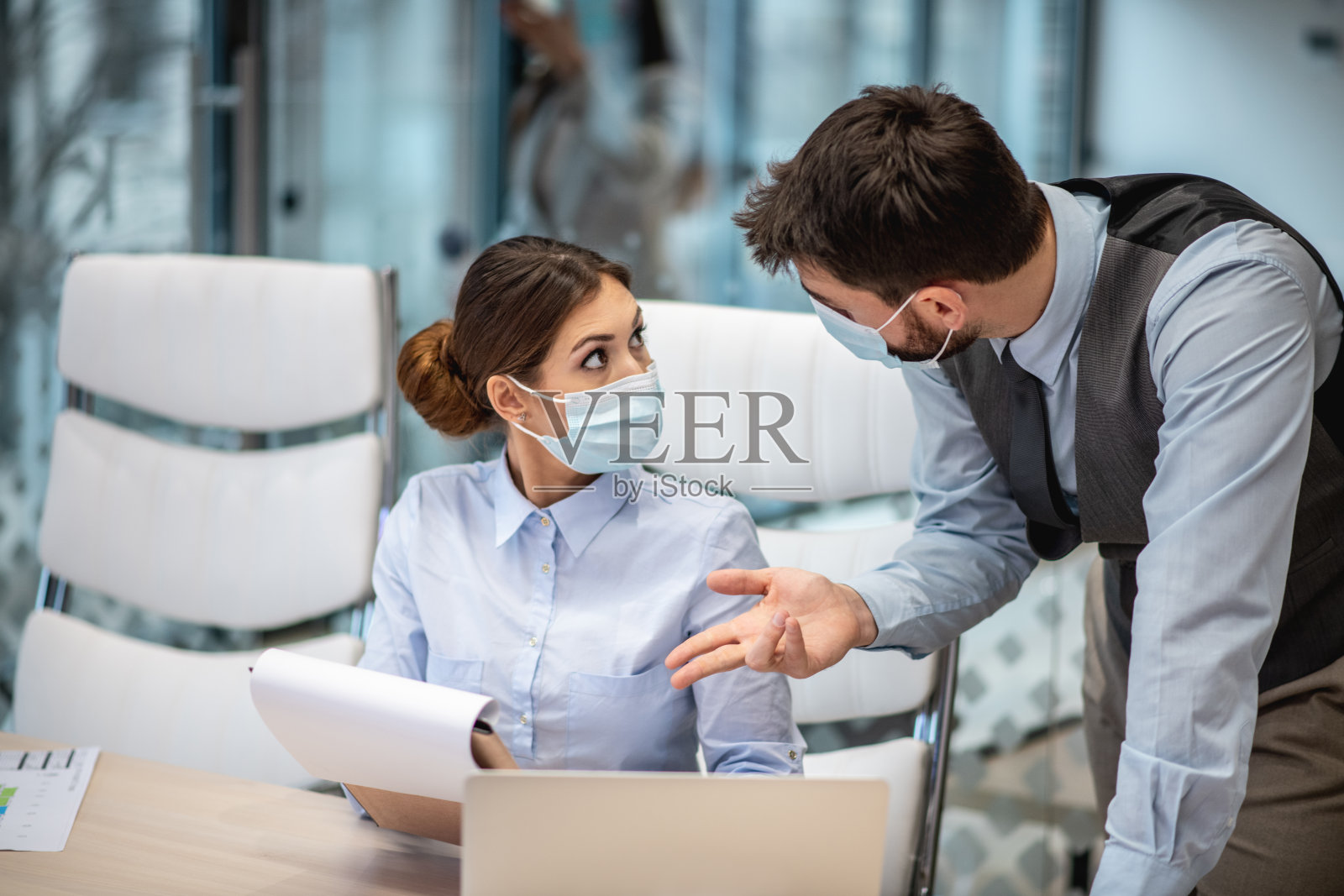 两个年轻的工人在他们的办公室谈论关于项目的问题。他们都戴着防护面具。照片摄影图片