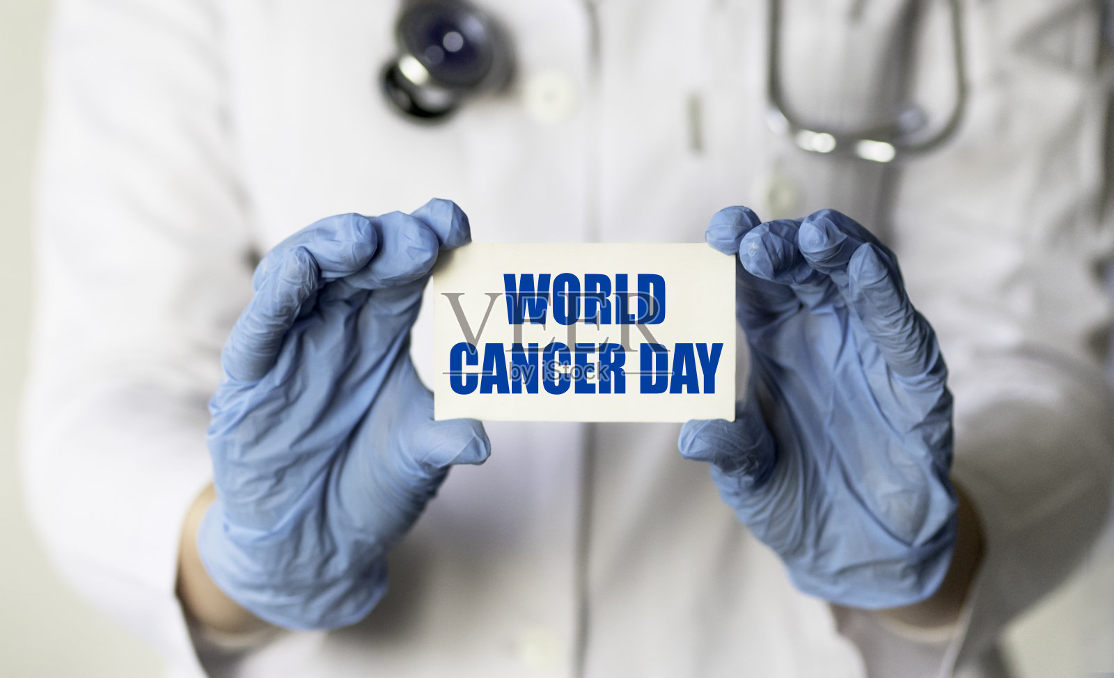 一位戴着手套的医务工作者手里拿着一张写着“世界癌症日”的卡片。医学概念。照片摄影图片