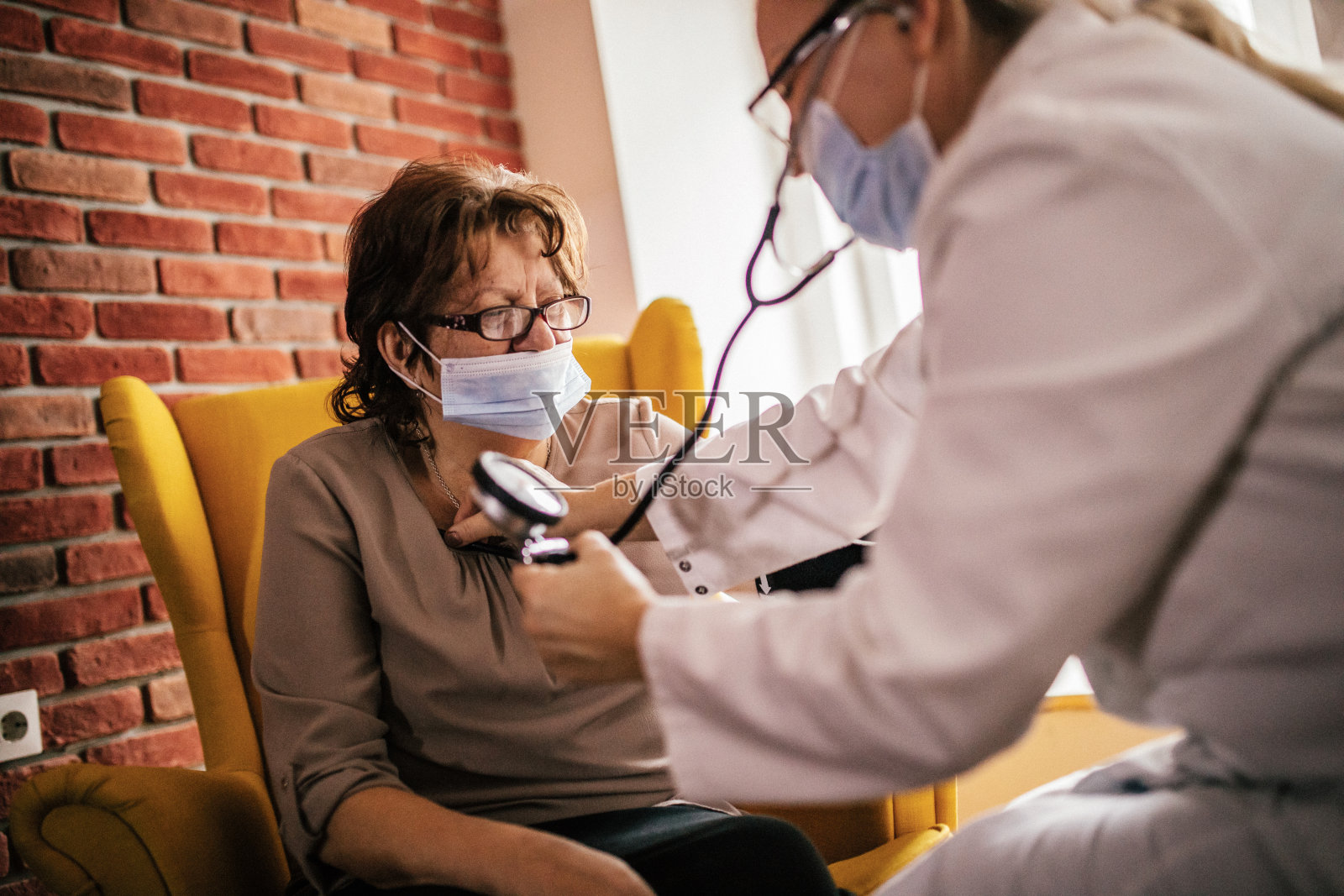 女医生和她的老病人在家访时戴上防护口罩。照片摄影图片