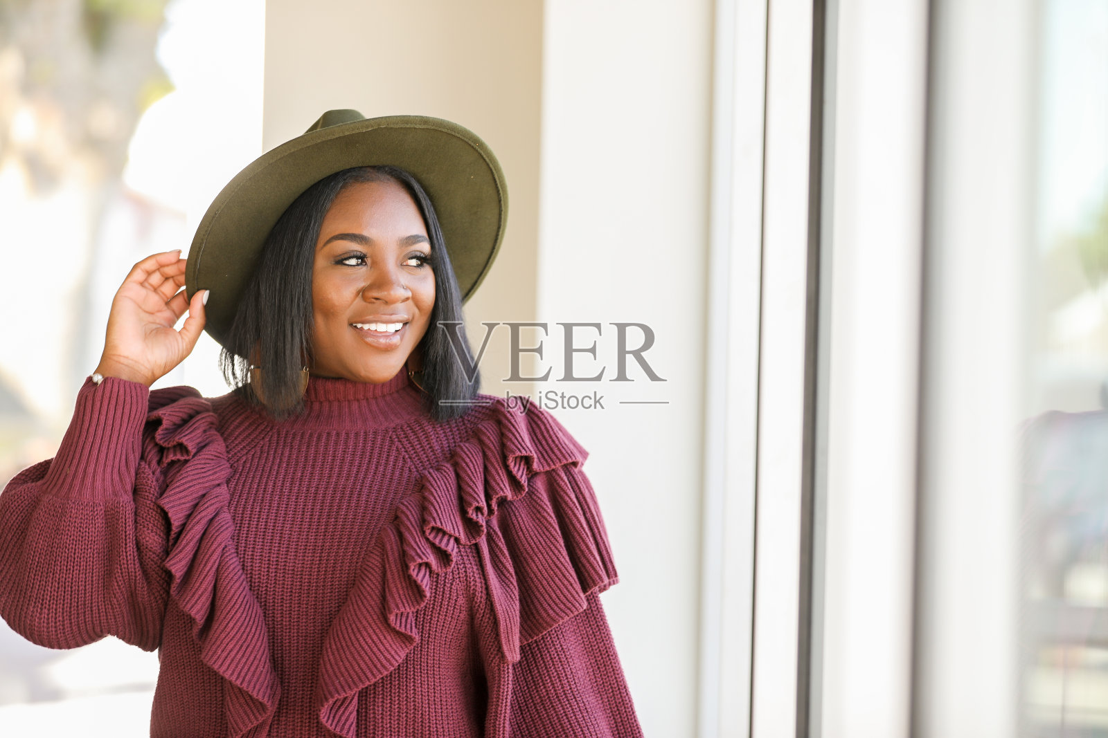 年轻女子戴着时髦的帽子,微笑着看着窗外照片摄影图片