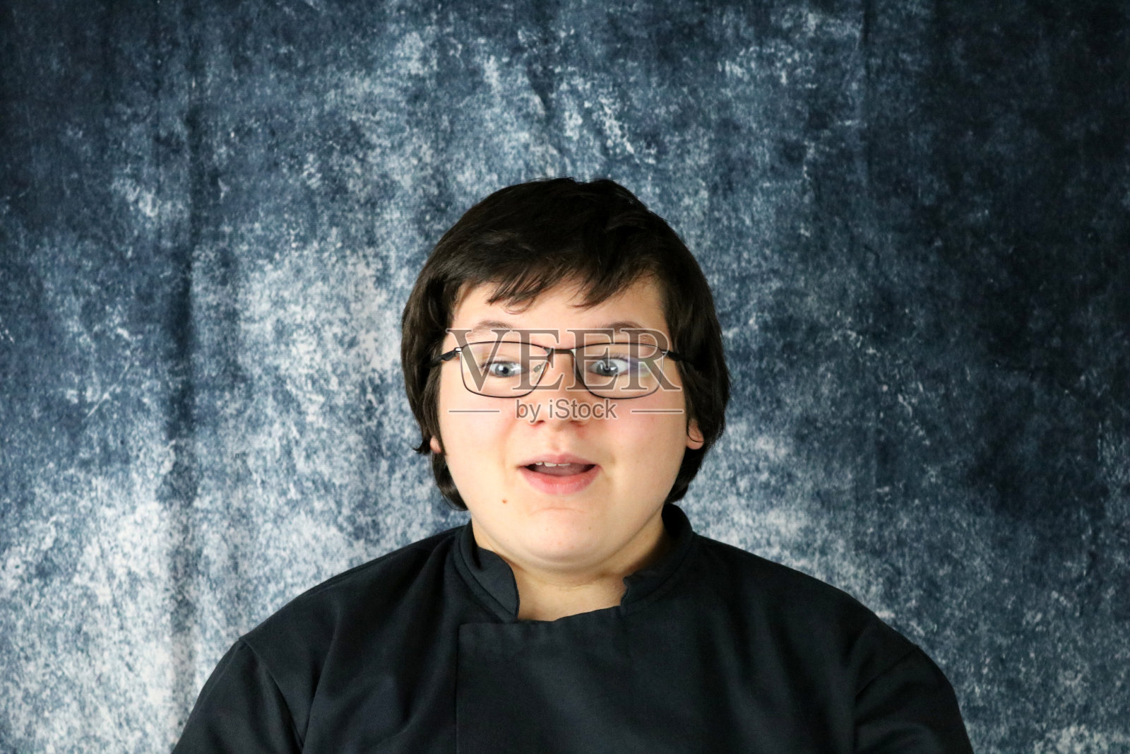 戴眼镜的年轻人惊讶的表情在蓝色的石磨背景照片摄影图片