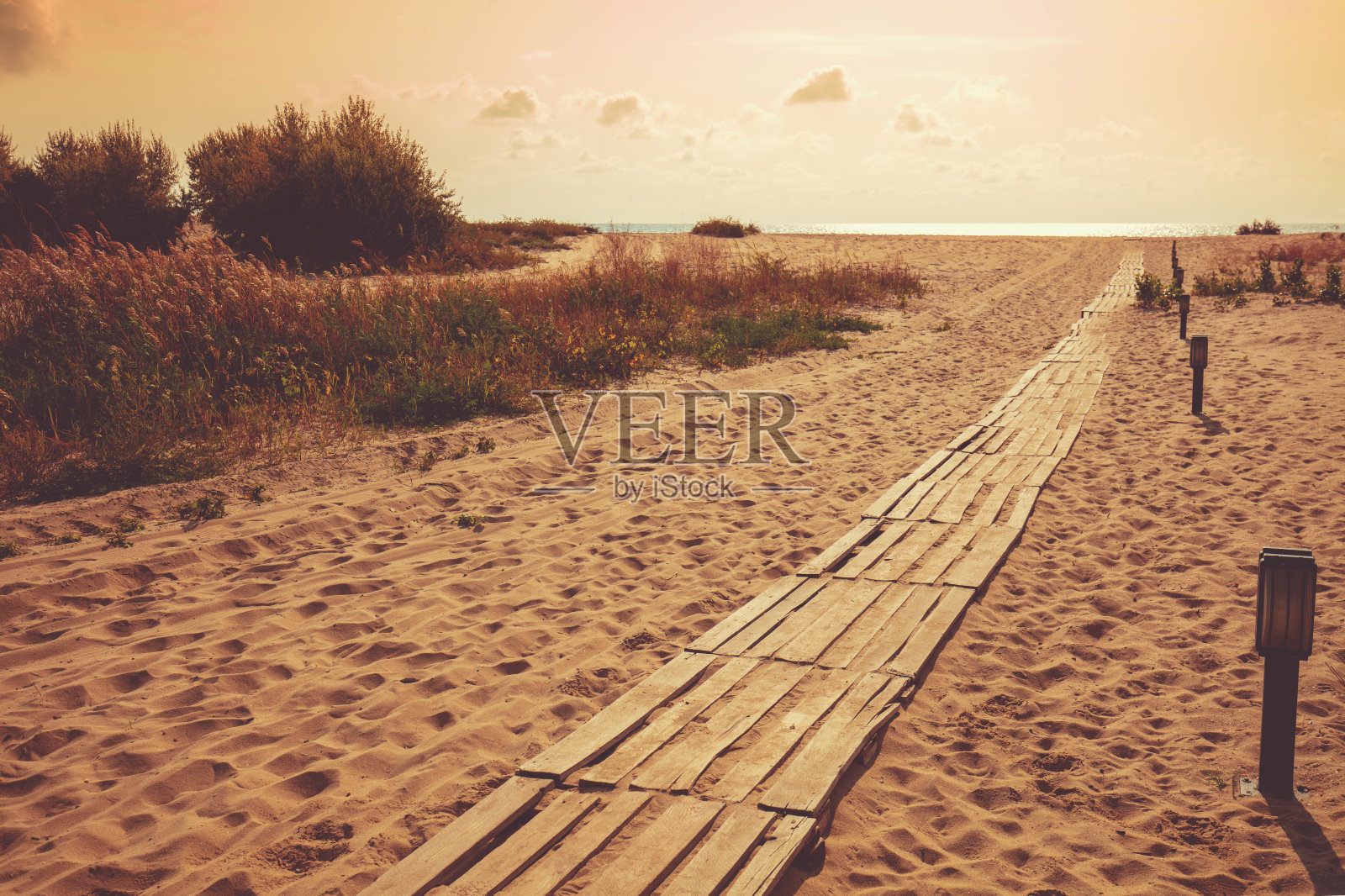 沙滩上的木栈道在落日的神奇光芒下。傍晚美丽的海景照片摄影图片