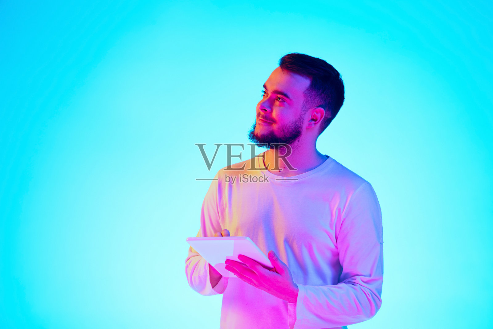 一个白人男子的肖像,在霓虹灯下的蓝色画室背景上。人的情感,面部表情,销售,广告的概念。照片摄影图片