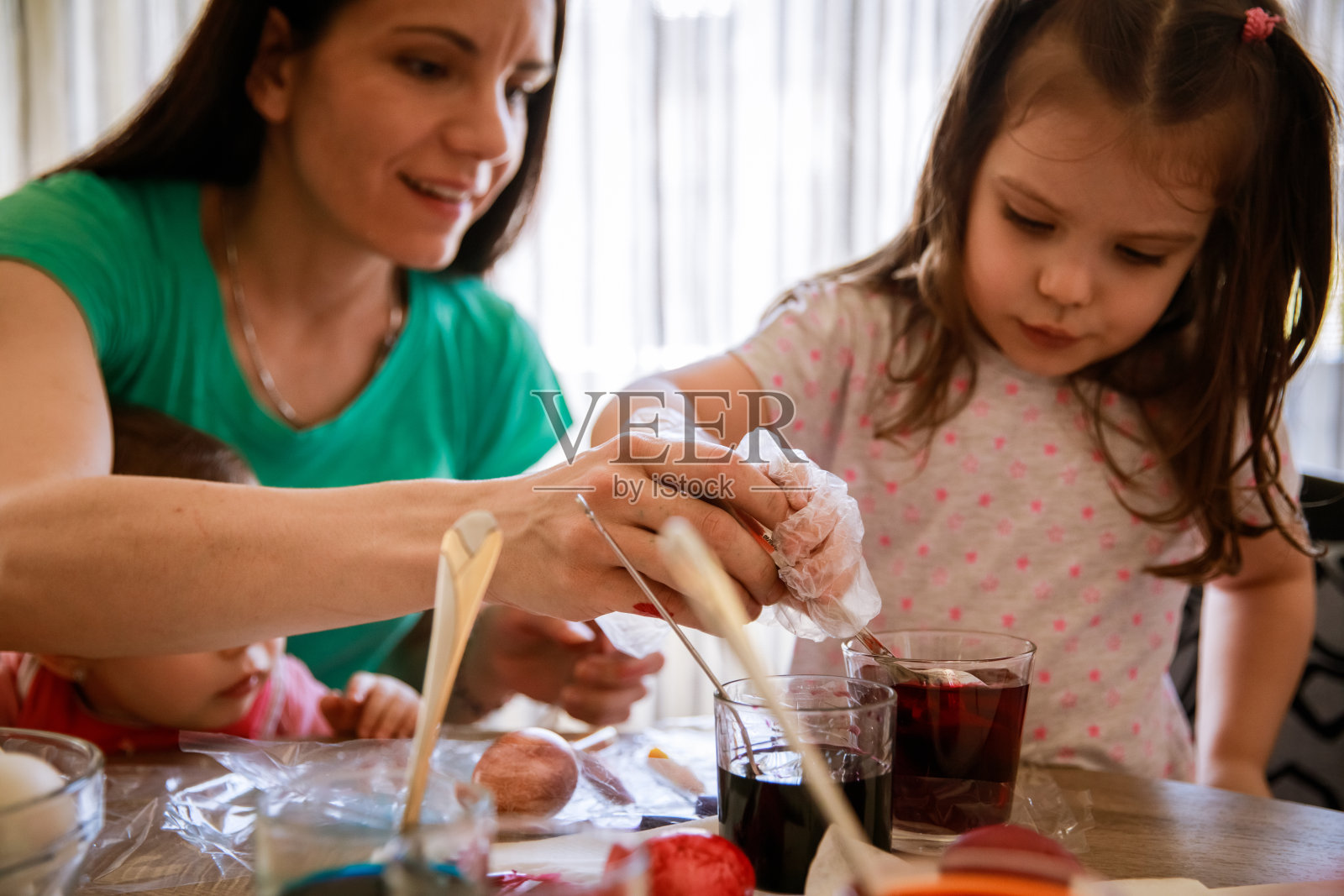 母亲帮助蹒跚学步的女儿为复活节染色照片摄影图片