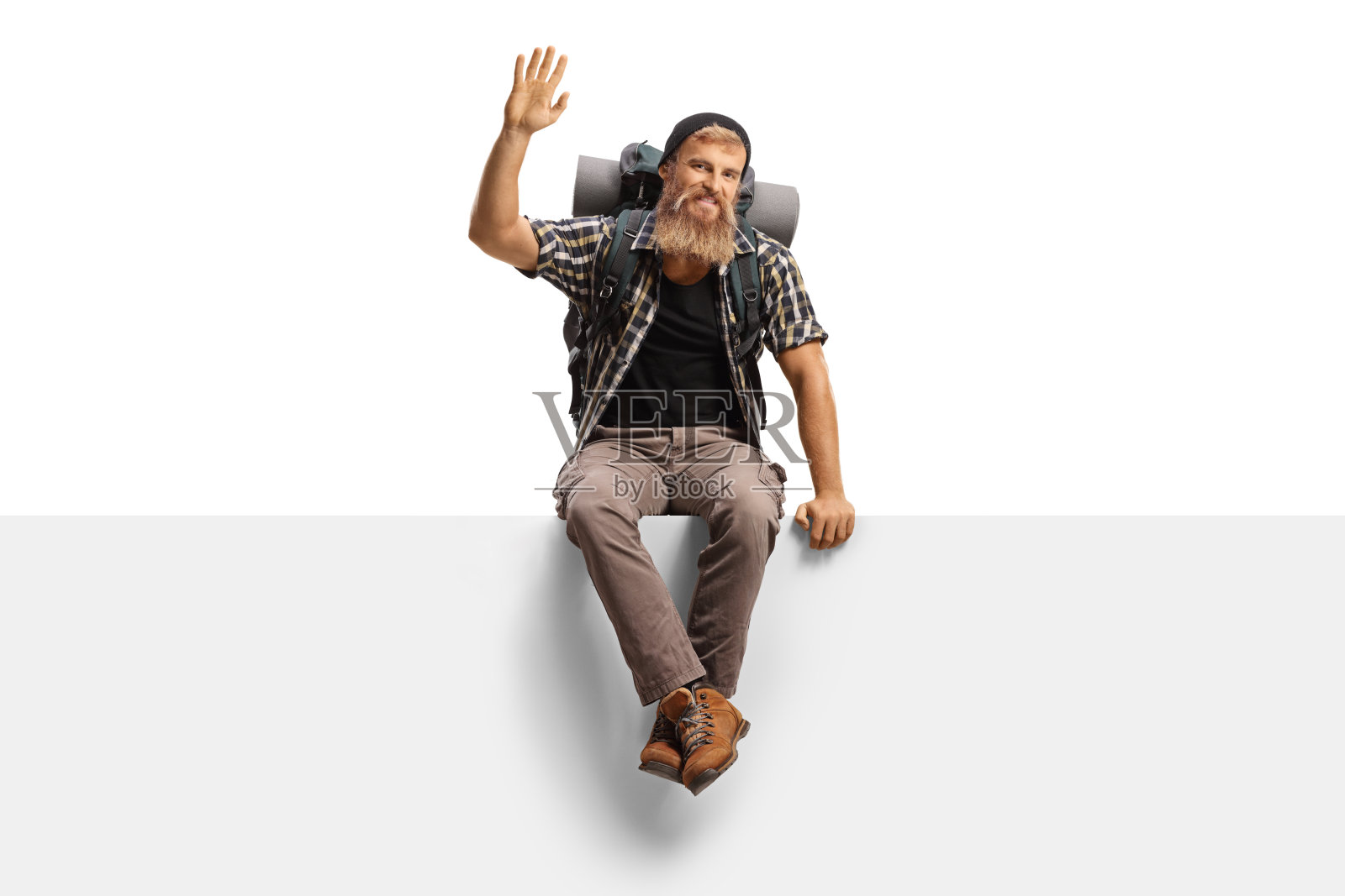 年轻的徒步旅行者背着背包坐在一个空白的面板上,对着镜头挥手照片摄影图片