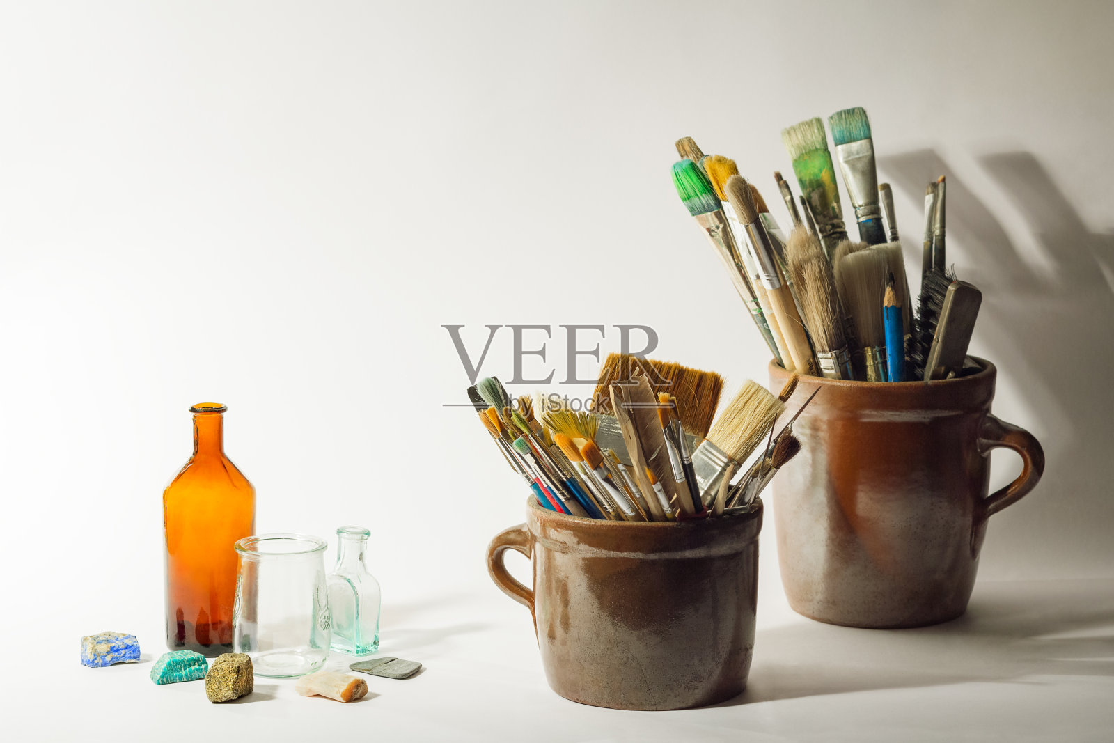 艺术的画笔,彩色的漂亮的石头,旧瓶子和绘画工具在旧陶瓷罐在白色的背景。艺术成分照片摄影图片