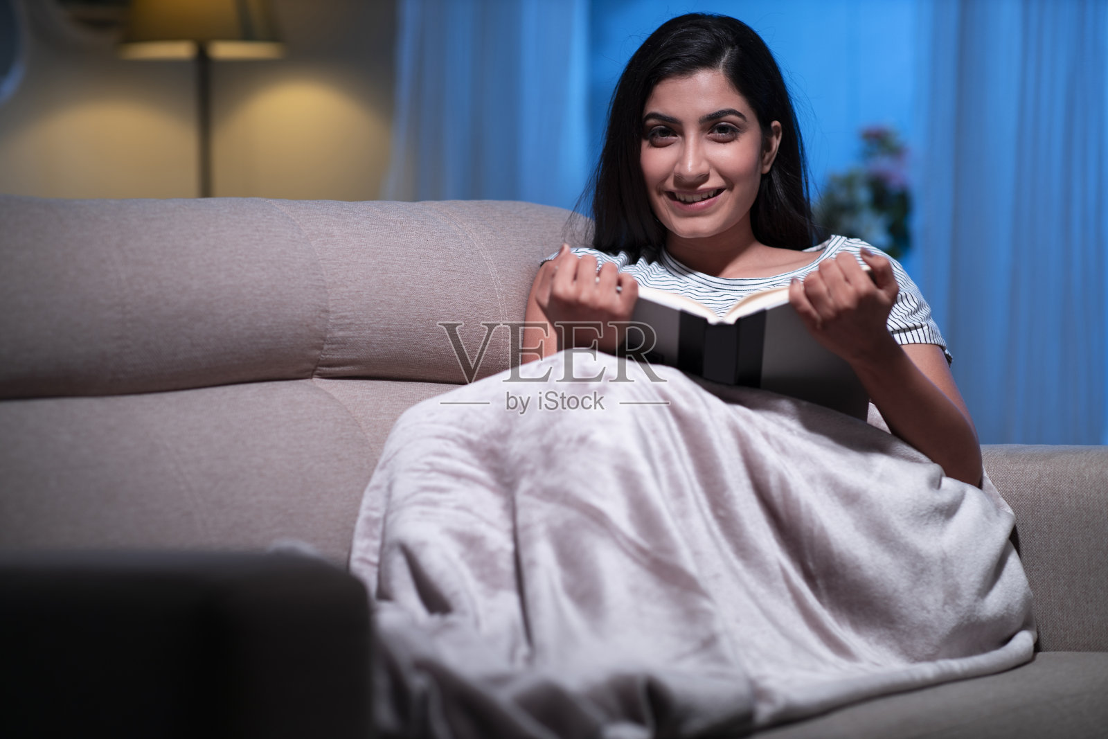 年轻女性坐在家里的沙发上看书照片摄影图片