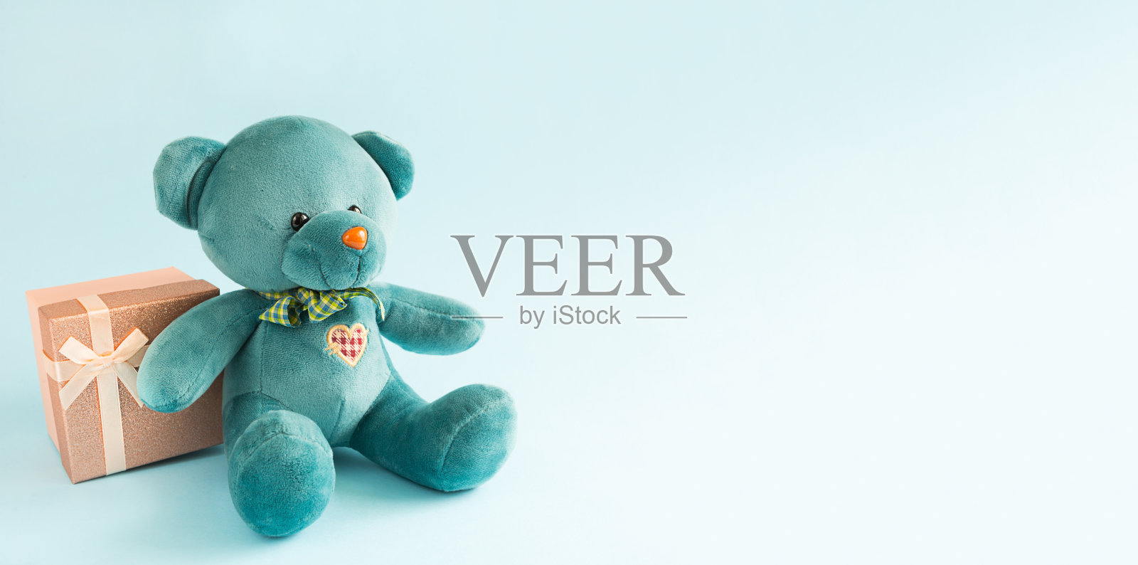 绿松石软泰迪熊与绣花心持有一个礼盒和一个蝴蝶结在蓝色的背景。孩子们的玩具。爱情,节日的礼物,爱情的宣言,情人节。本空间照片摄影图片