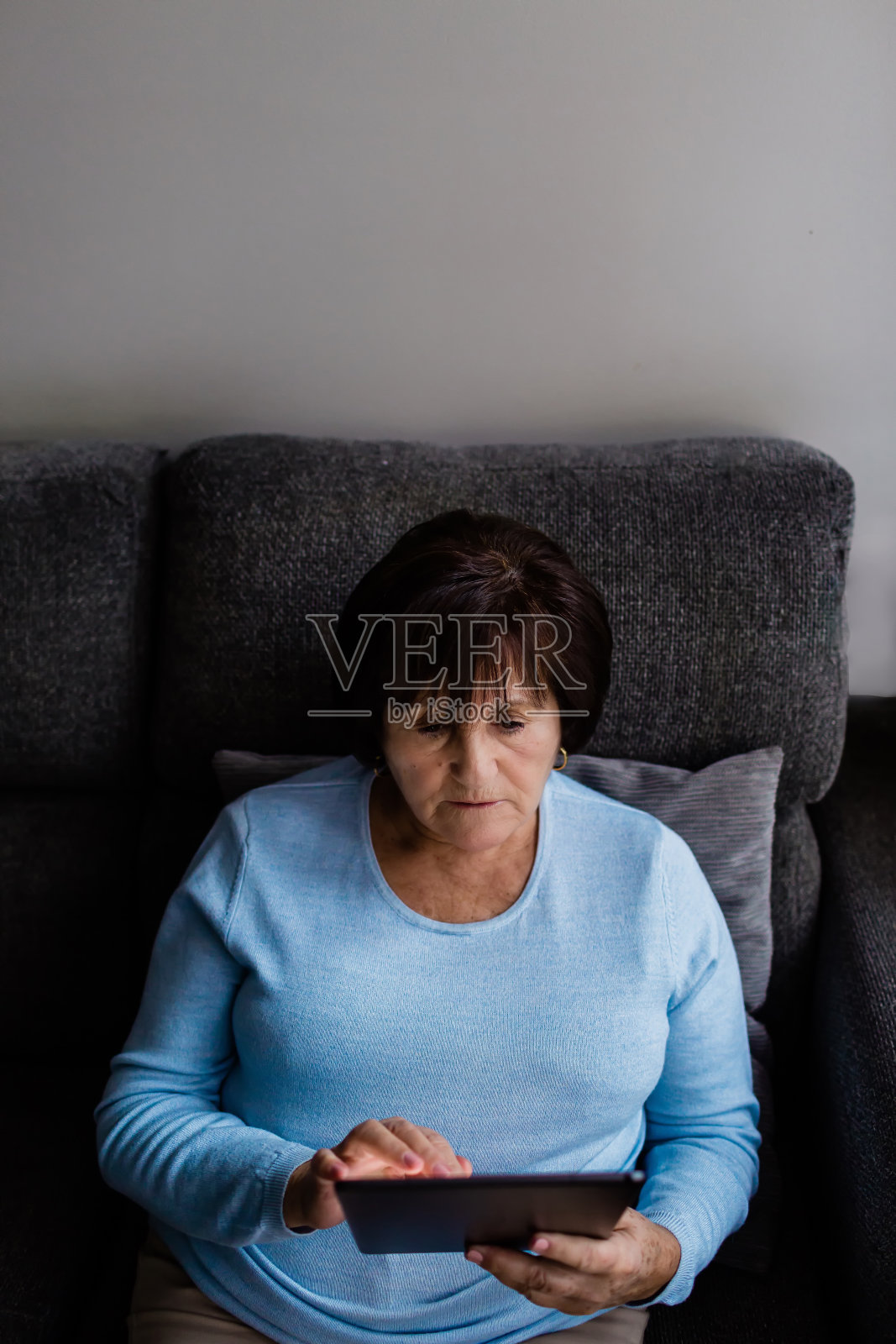 一位资深女性坐在家里的沙发上用平板电脑阅读照片摄影图片
