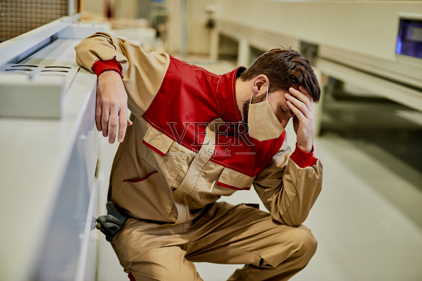 工厂工人戴着口罩感到不适,在生产设施中痛苦地抱着他的头。照片摄影图片