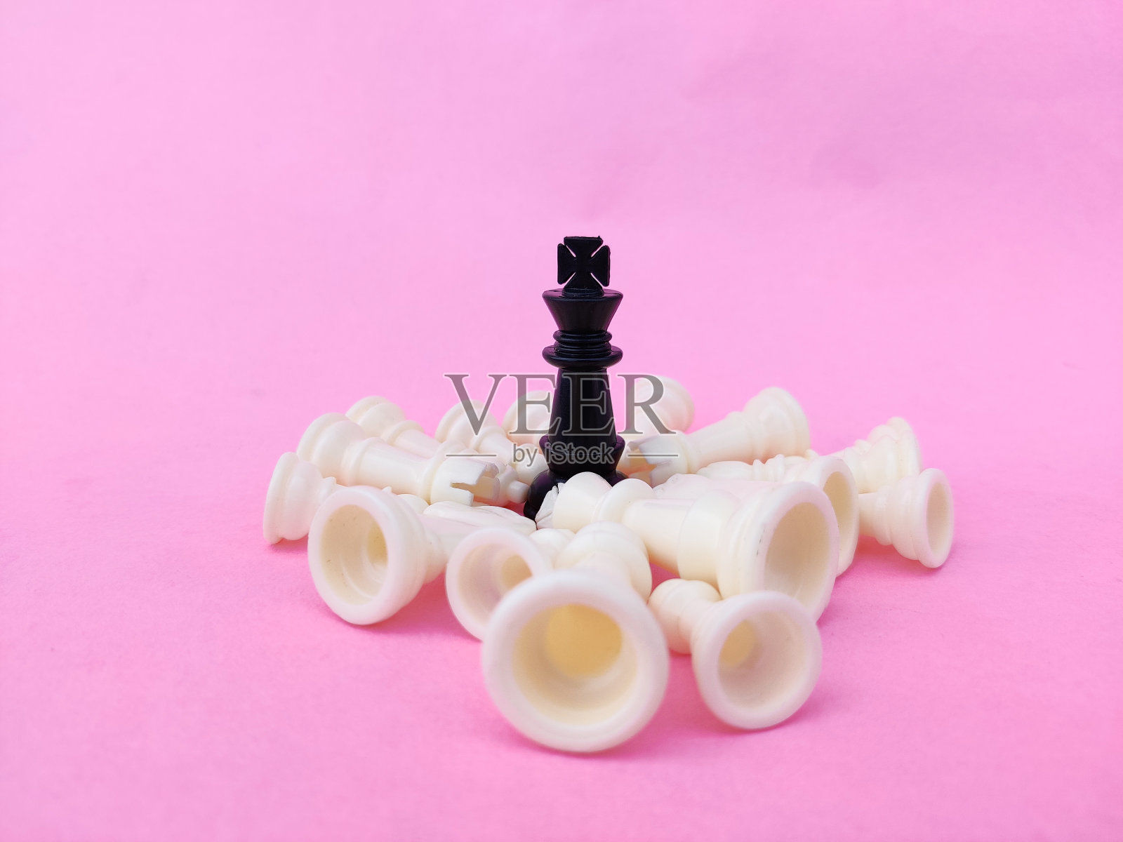 黑棋王被倒下的白棋子包围着。粉红色的背景。经营理念照片摄影图片