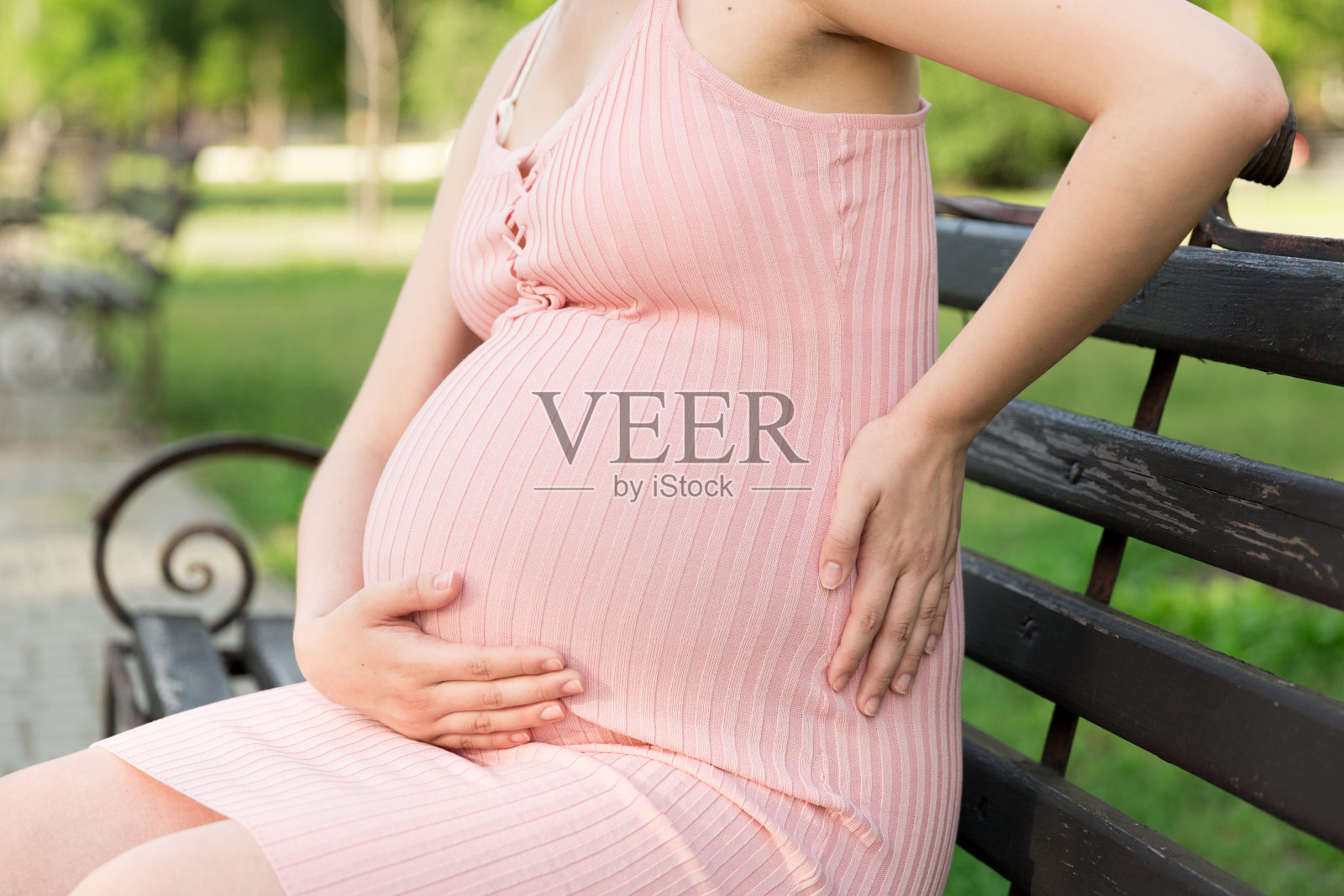 一个怀孕的年轻女人坐在公园的长椅上,扶着受伤的肚子。怀孕和生育。怀孕期间背痛照片摄影图片